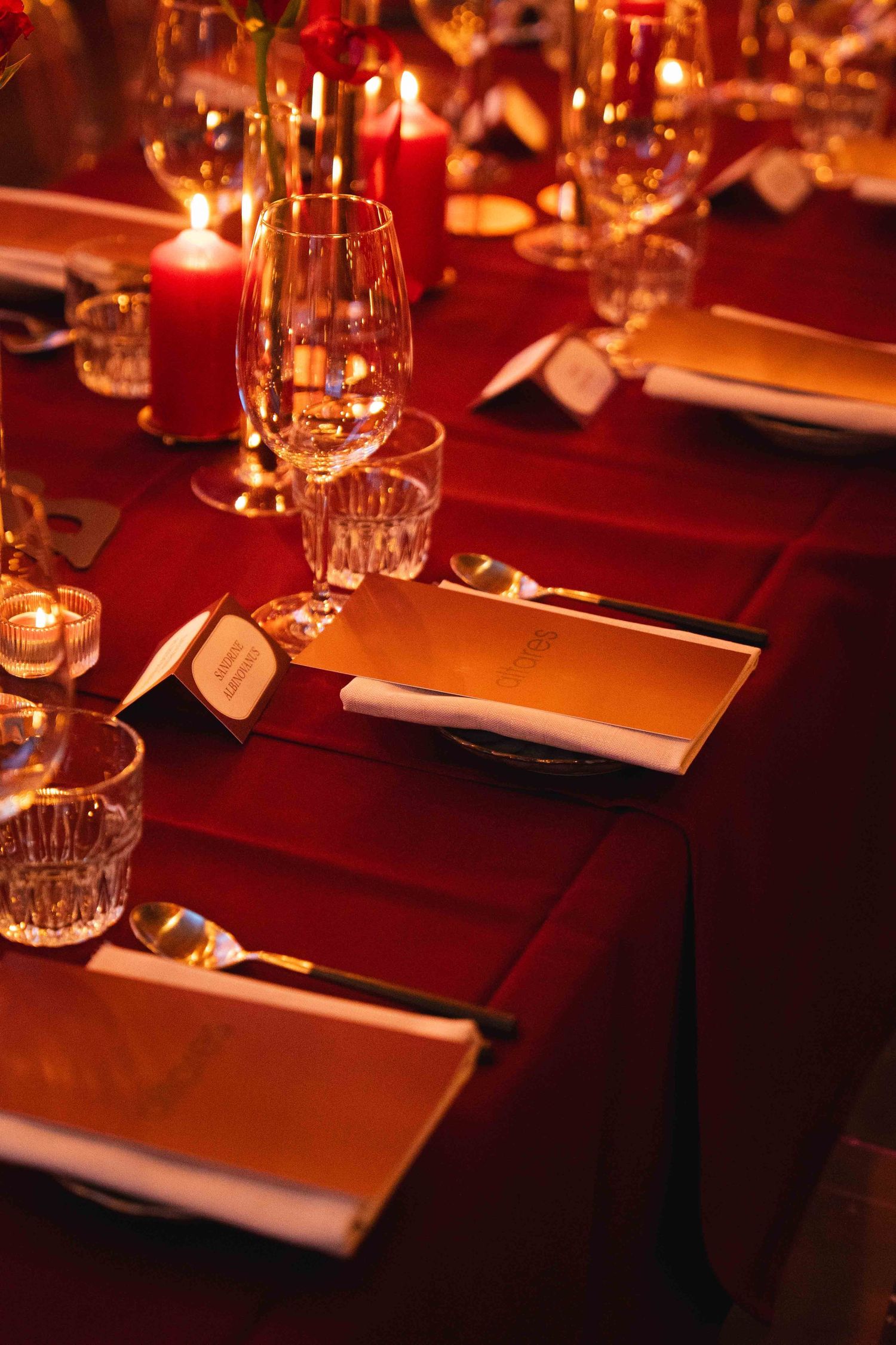 Elegant red table setting with crystal glasses, candles, gold menus, and place cards for a formal dinner event.