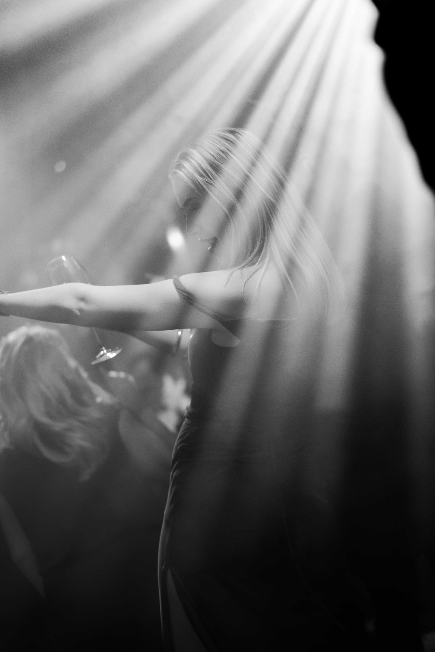 Black and white photo of a blonde woman performing on stage under dramatic spotlight rays.