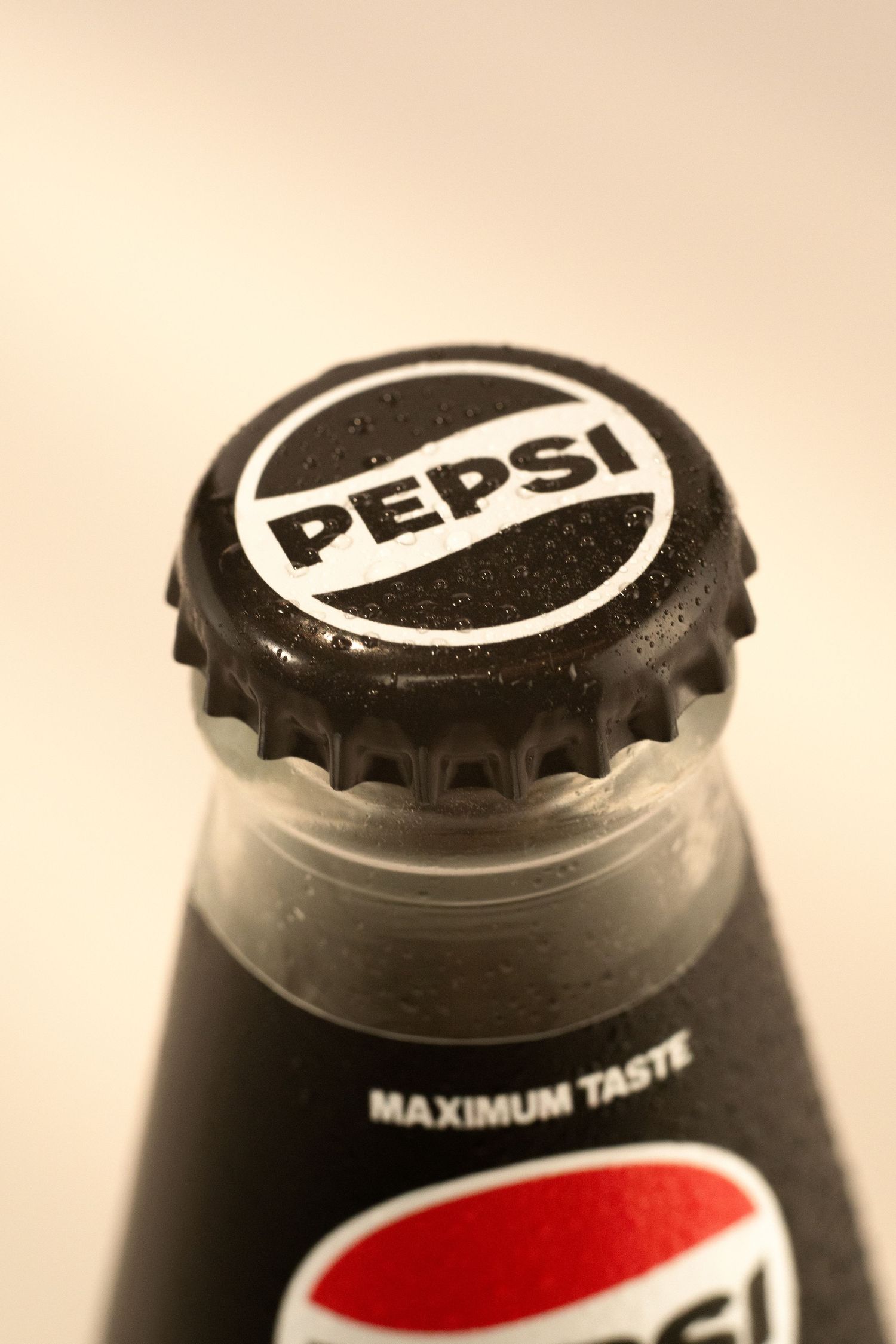 Close-up of a Pepsi bottle cap on a dark glass bottle with Maximum Taste label visible.