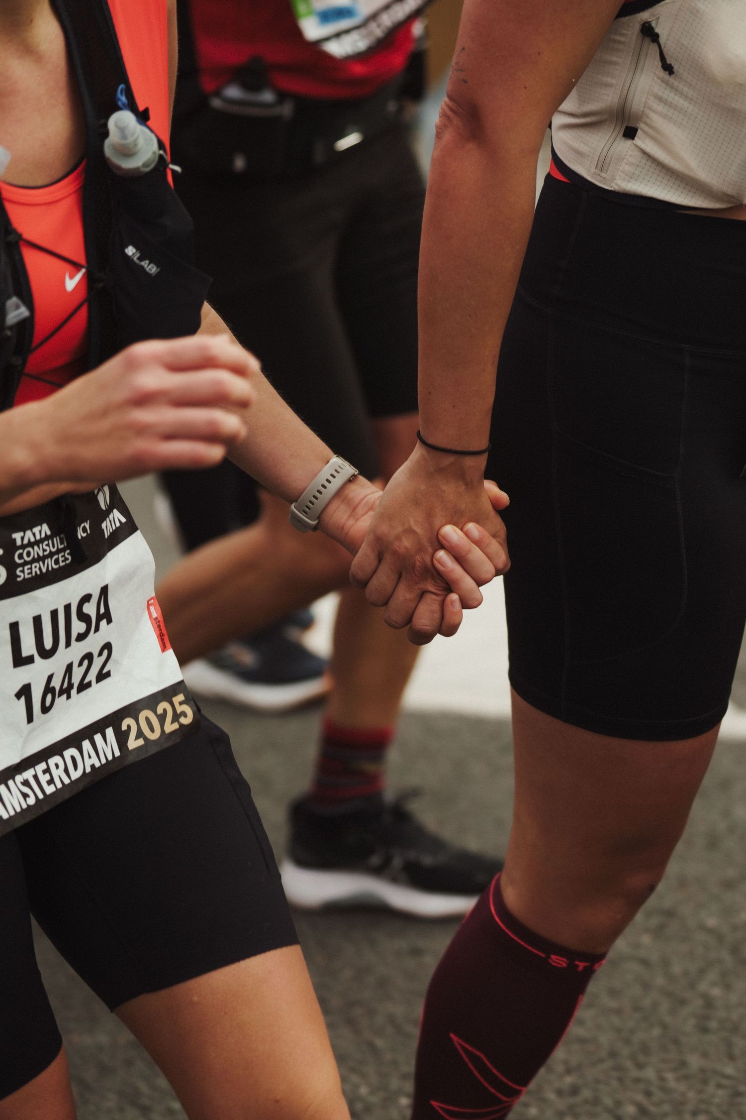 Close-up of runners holding hands during Amsterdam marathon showing race number.