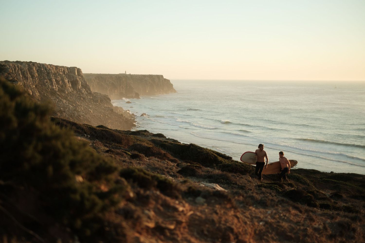 Surfers overlooking coastal cliffs and ocean at sunset.