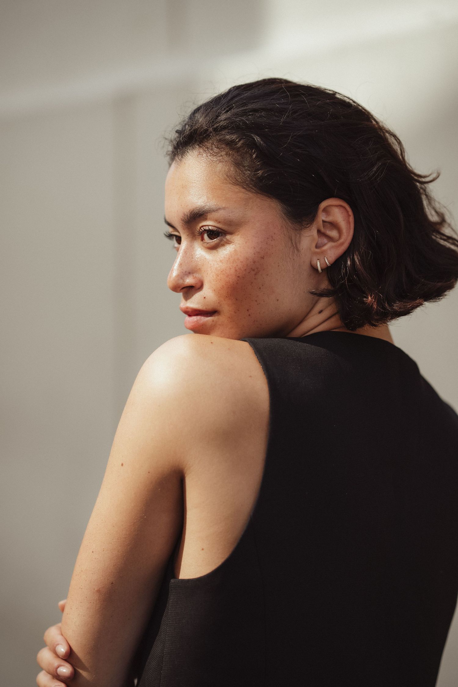 Young woman with freckles in black sleeveless top glancing over shoulder, natural light portrait.