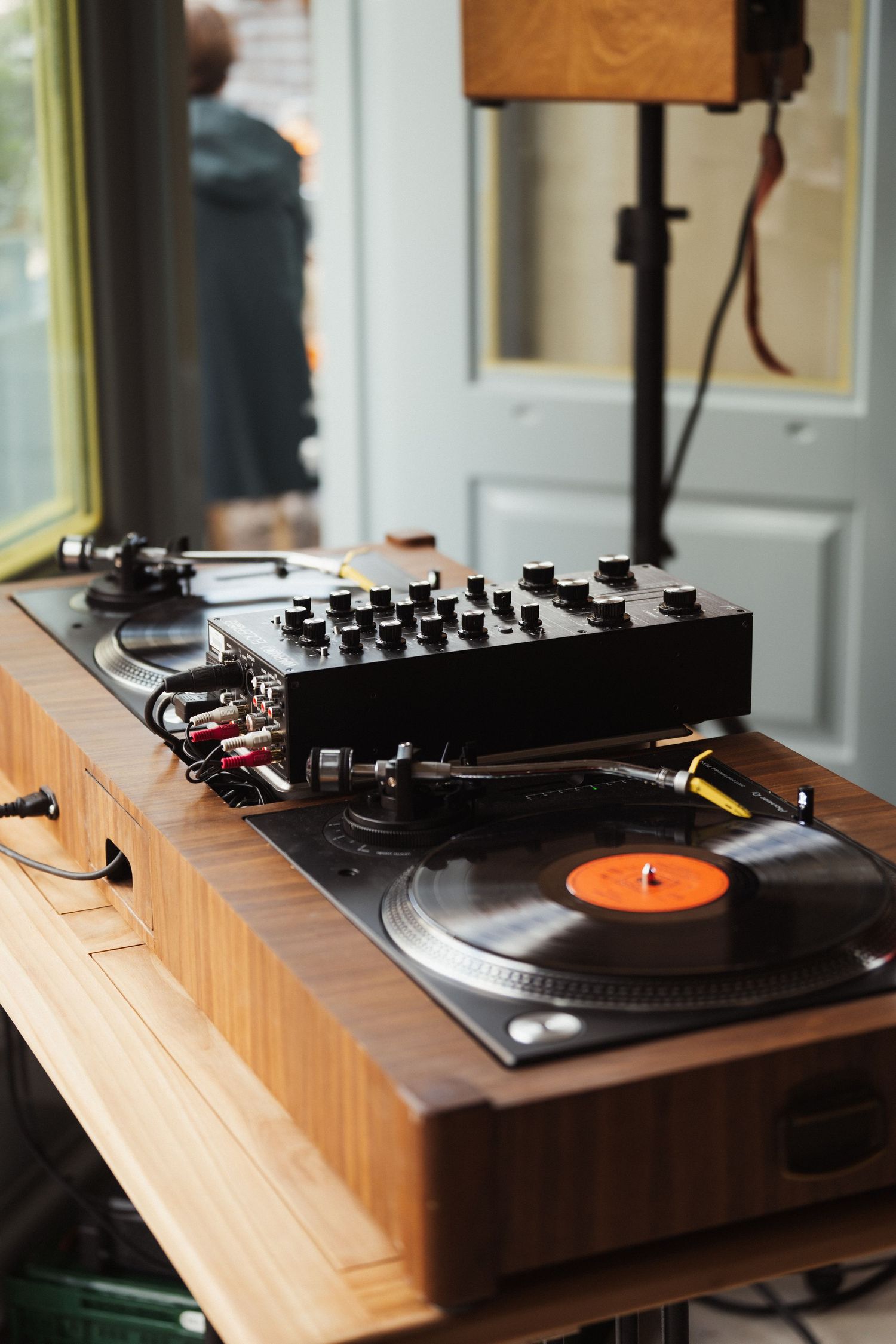 Vintage turntable with vinyl record and DJ mixer on wooden table in a cozy music studio setting.
