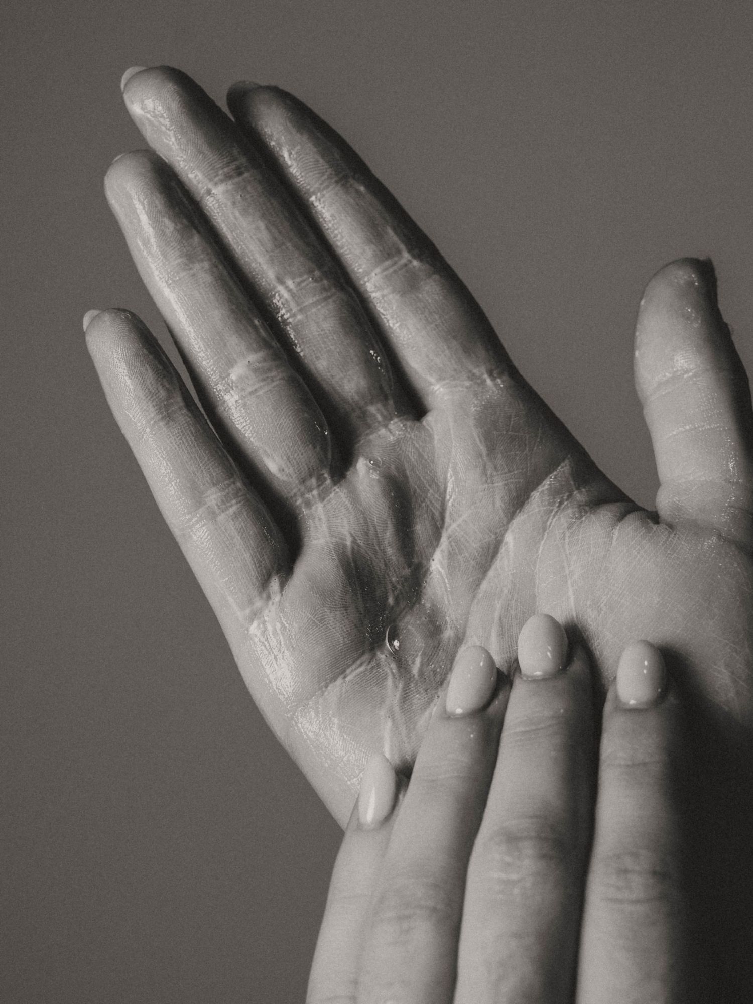 Black and white close-up of two hands with lotion being applied, showing detailed skin texture and moisture.
