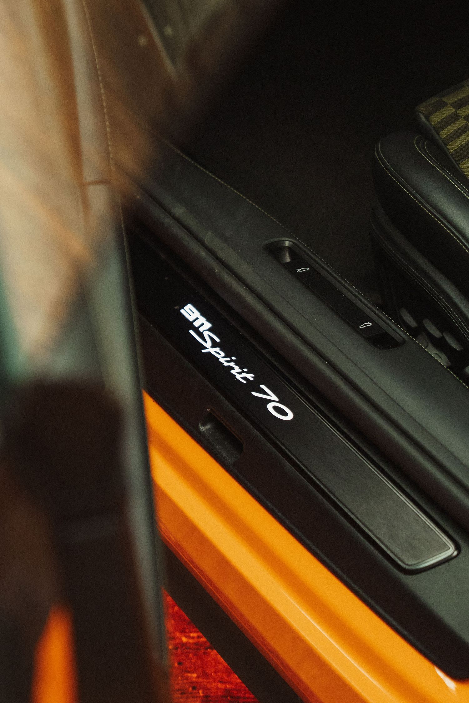 Close-up of illuminated BTSpirit 70 door sill plate in a luxury sports car with orange accents.