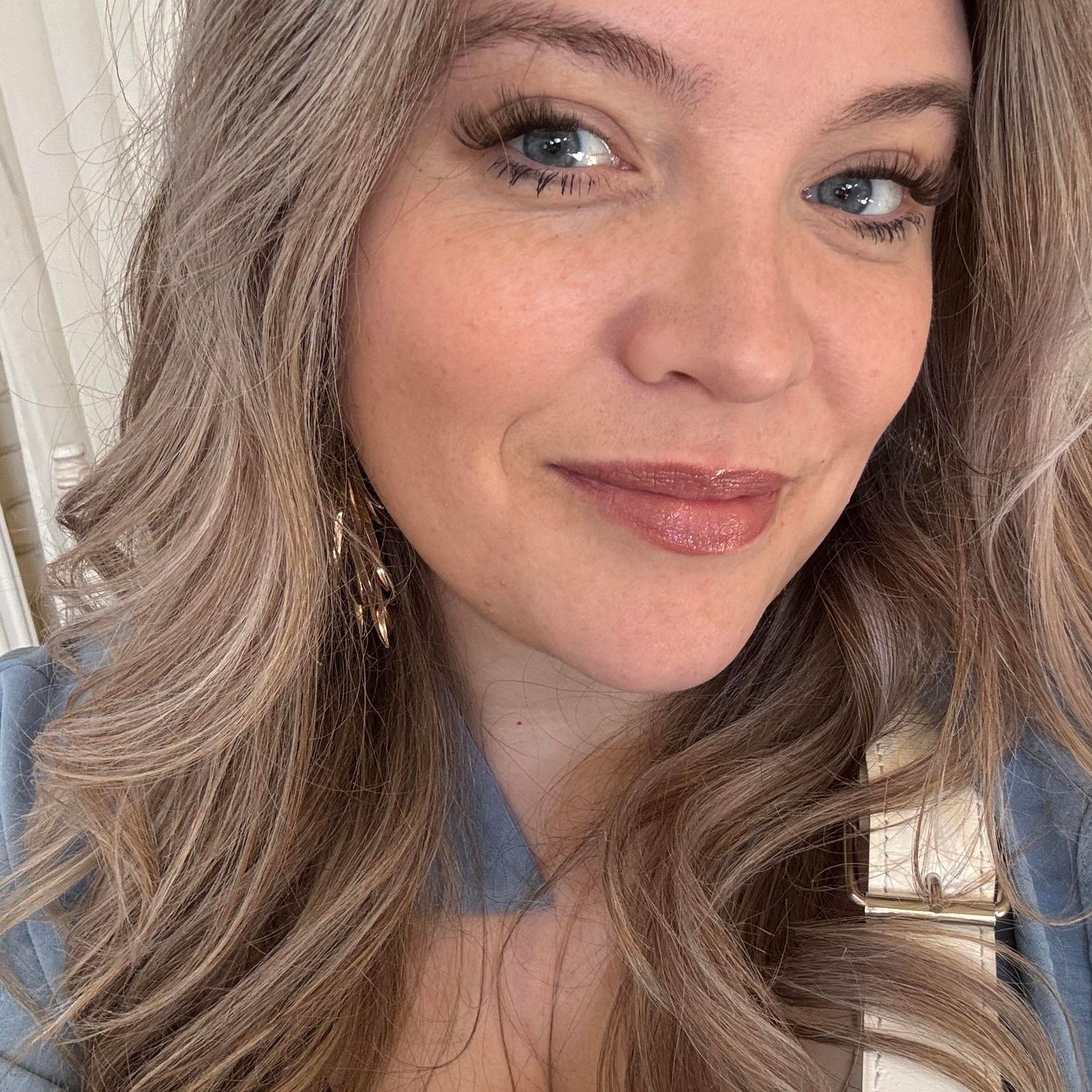 A close-up selfie showing silver-blonde hair, natural makeup, and a blue collar.