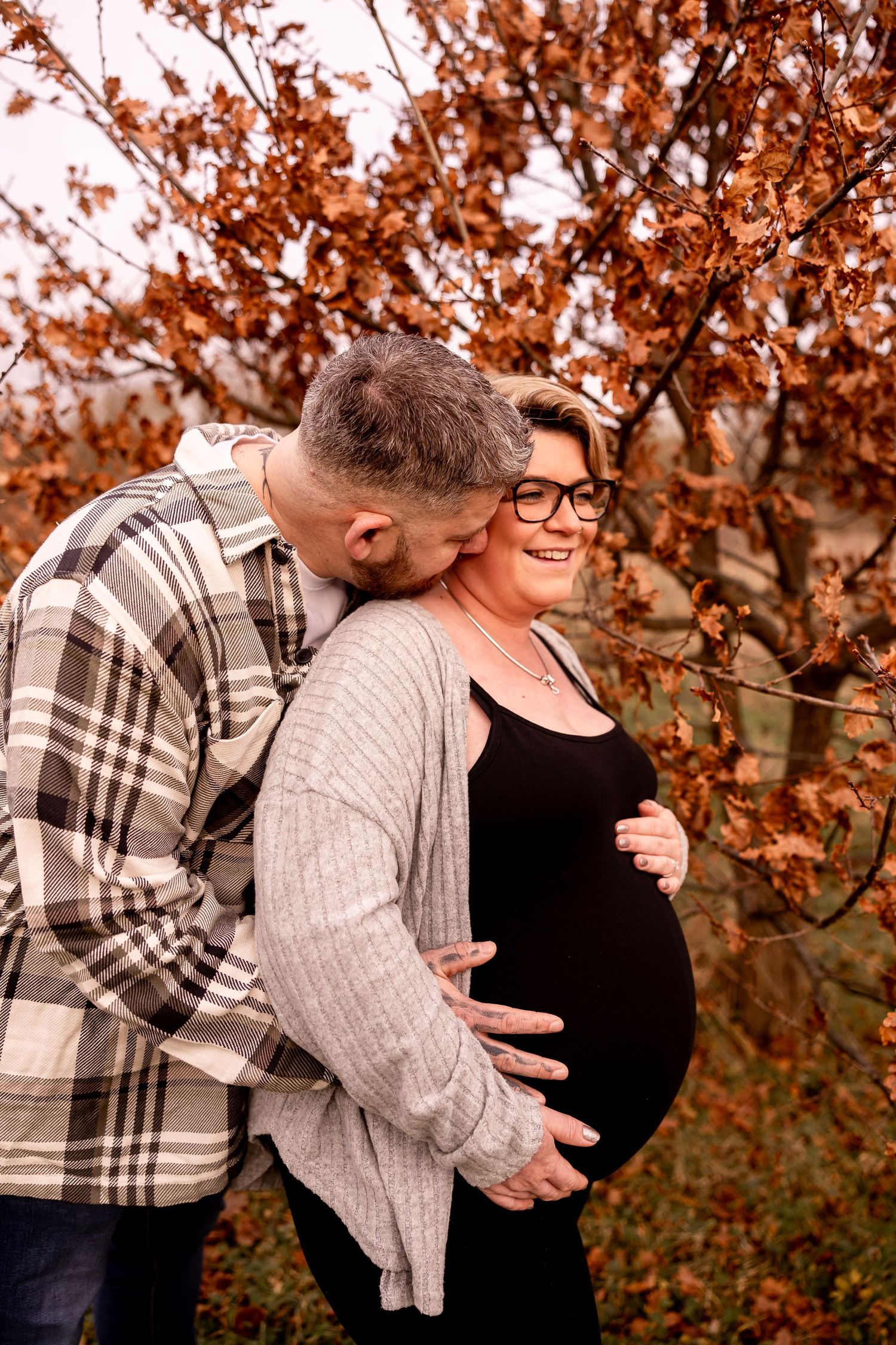 Autumn maternity photo with couple among orange leaves.