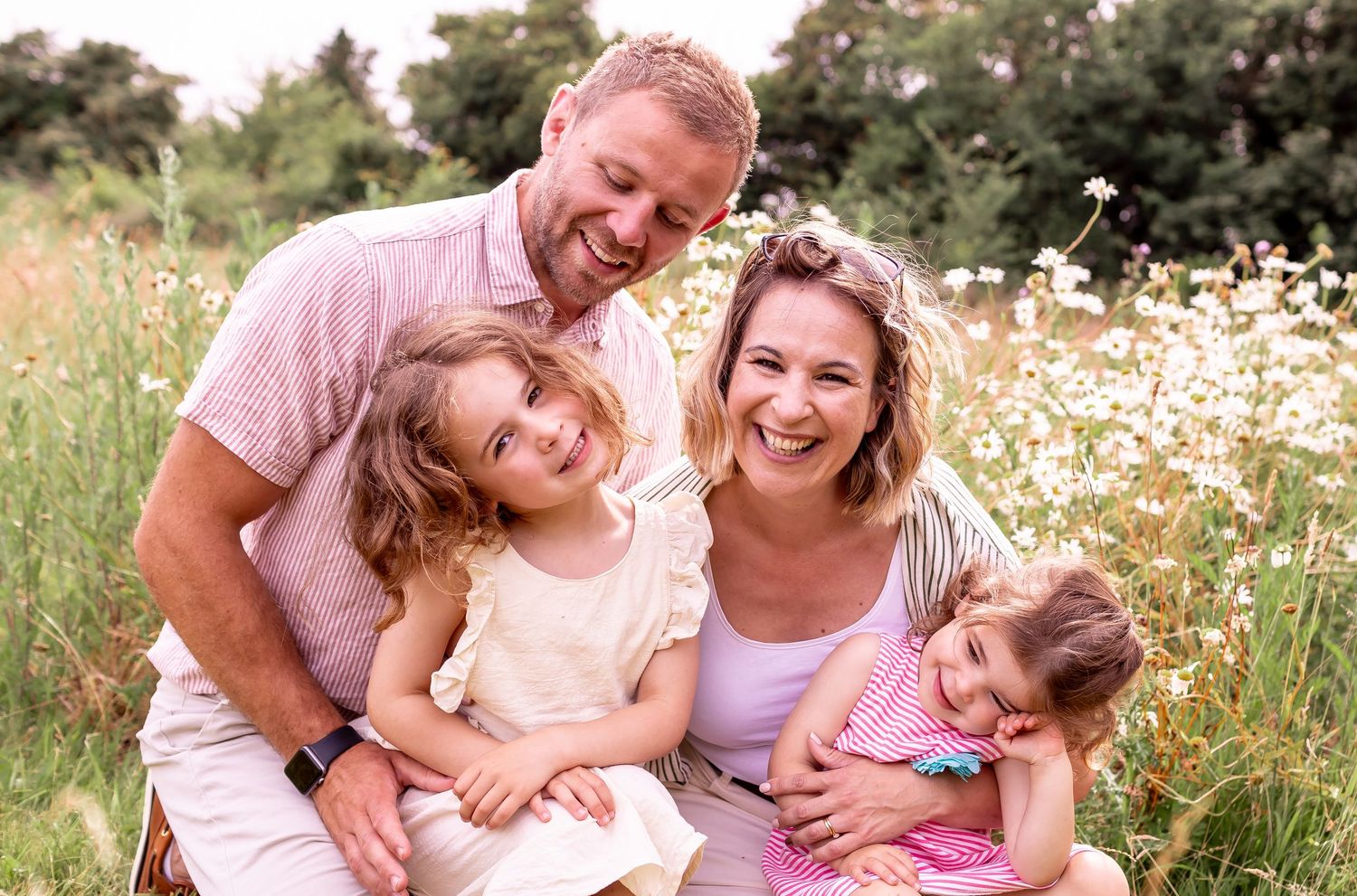 A joyful family moment captured in a wildflower meadow filled with white daisies on a sunny day.