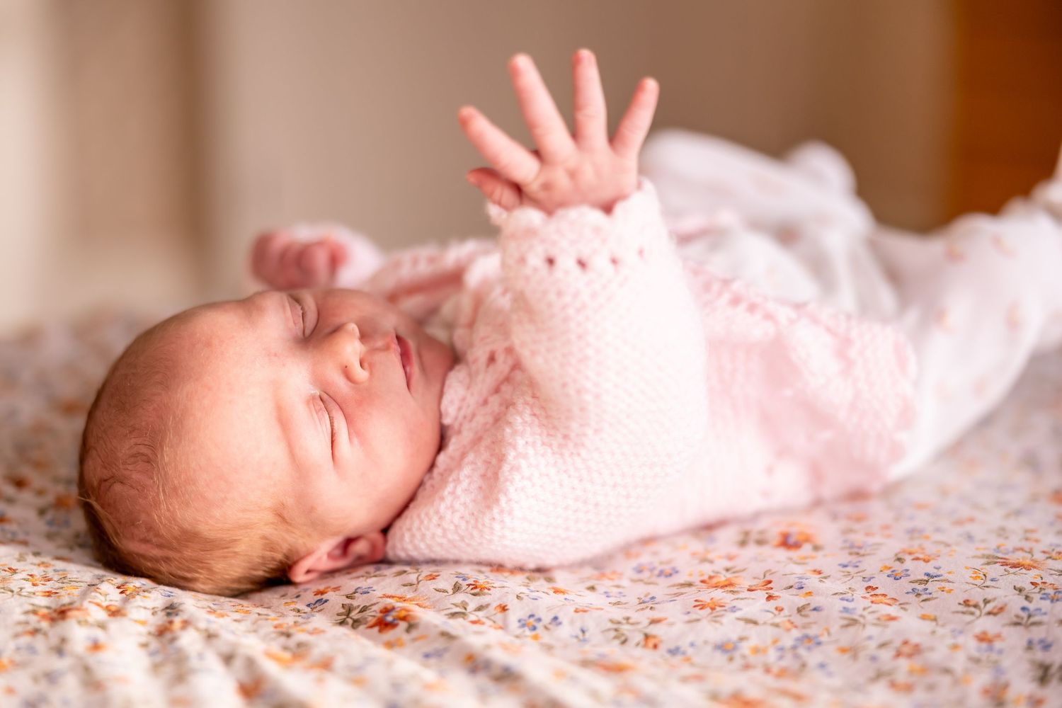 Newborn baby sleeping peacefully on floral bedding in soft pink tones.