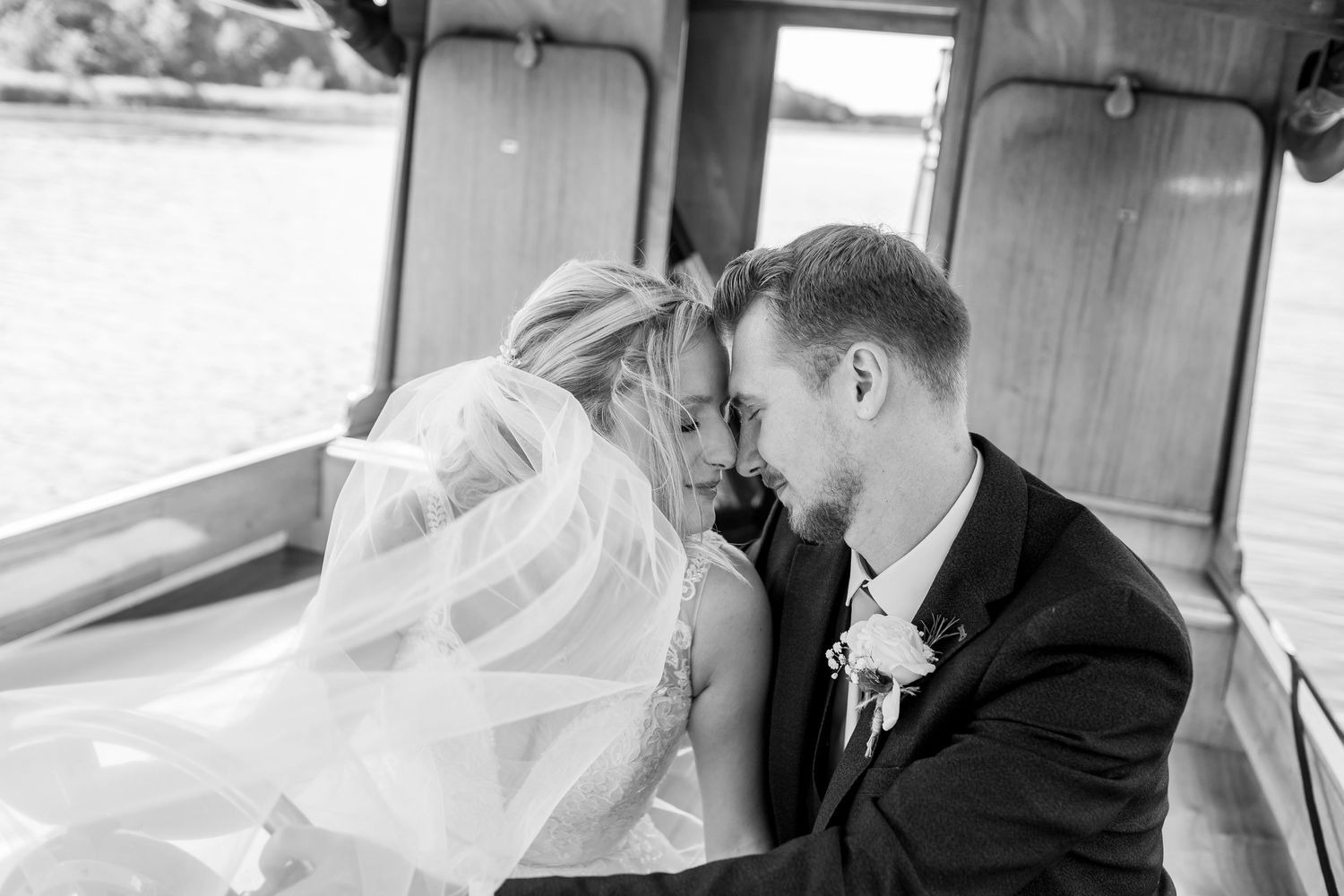 Black and white photo of newlyweds sharing an intimate moment on a boat with veil flowing in the breeze.