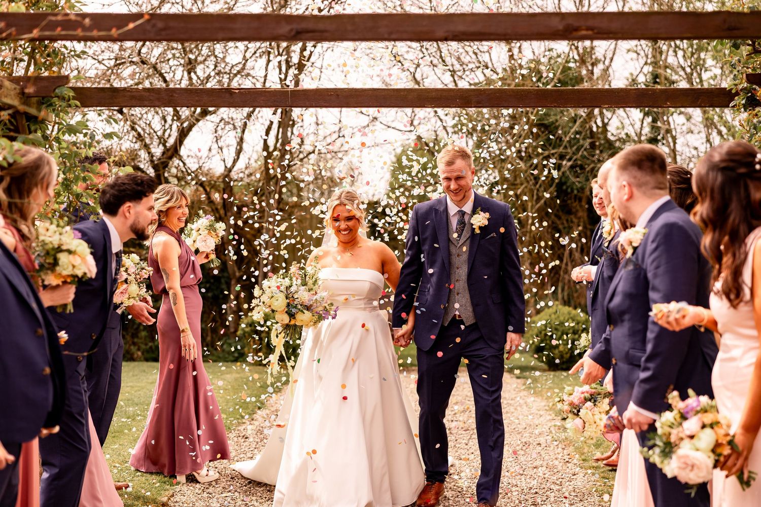 Wedding party celebrates outdoors with guests in a garden setting during golden hour.