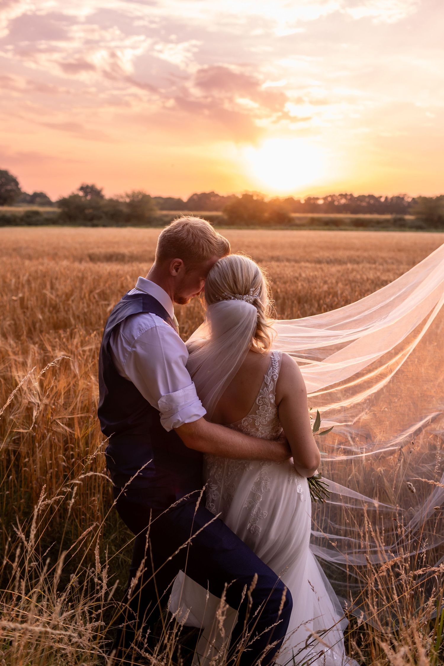 Romantic sunset photoshoot in a wheat field with flowing veil and warm golden light.