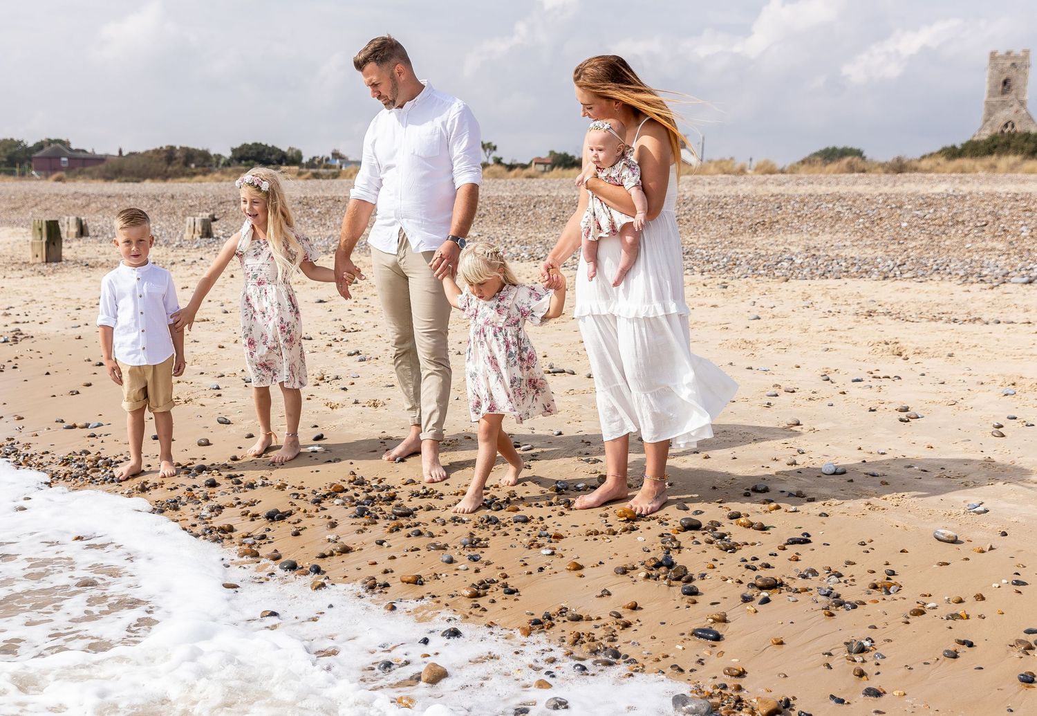 Family beach photoshoot with people walking along the shoreline in white summer attire.