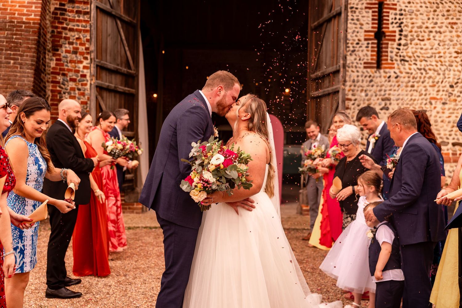 Wedding guests gather outside a rustic brick venue for post-ceremony celebrations.