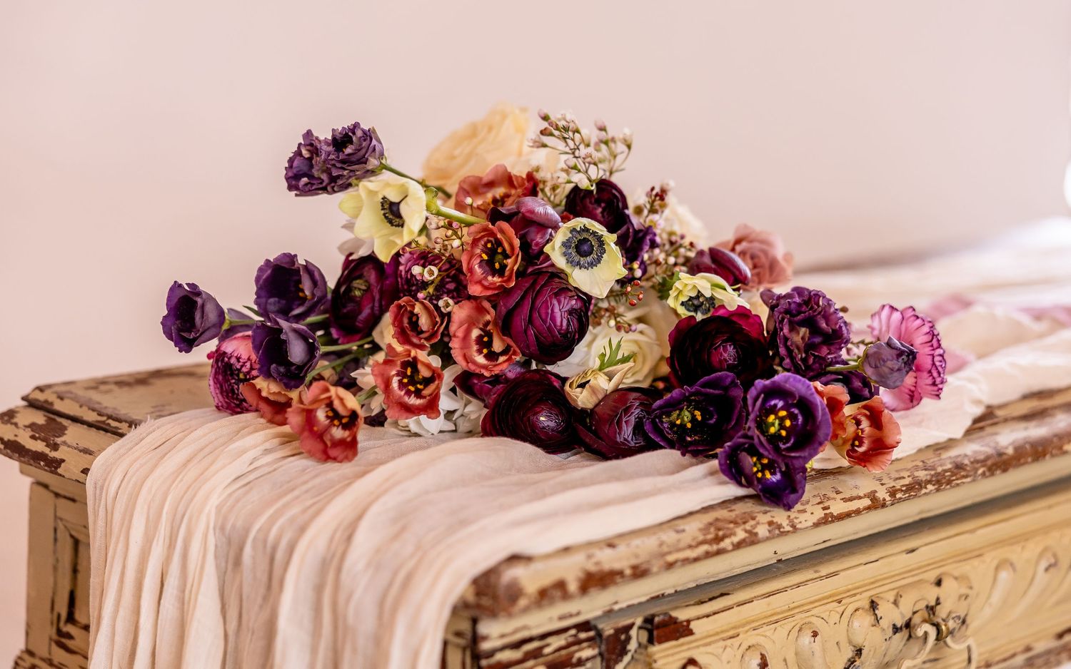 Vintage table decorated with rich purple and burgundy flowers and flowing fabric runner.