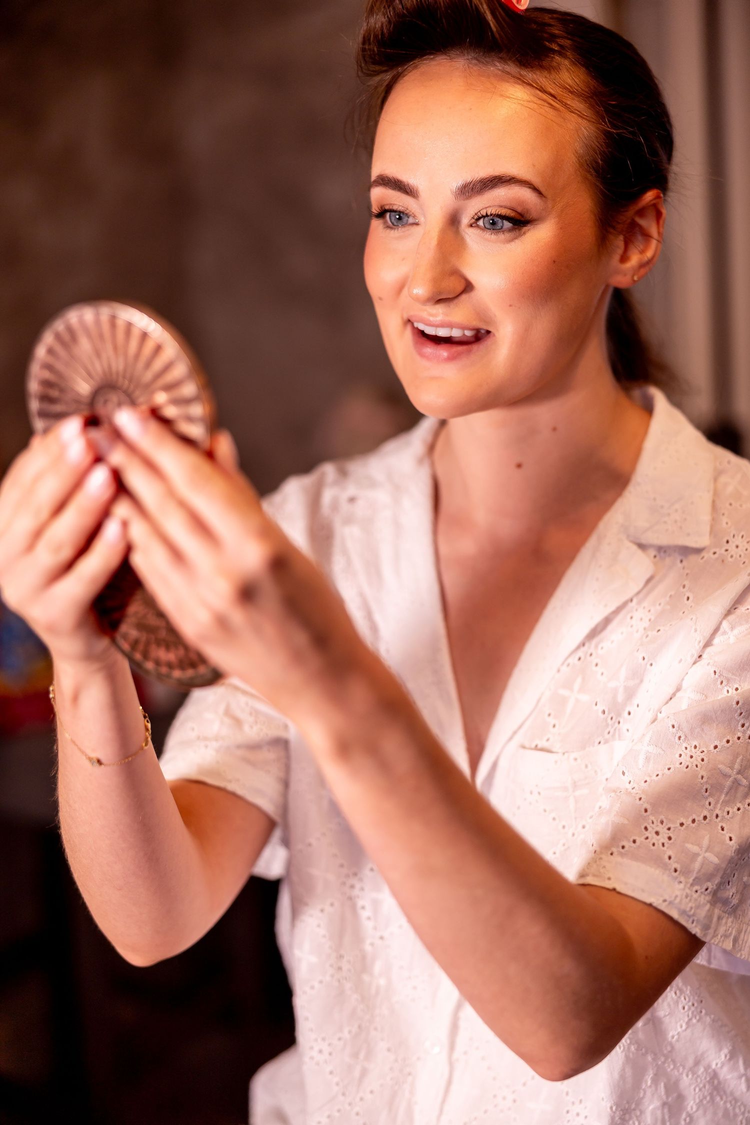 Person in white dress holding a decorative fan during wedding preparations.