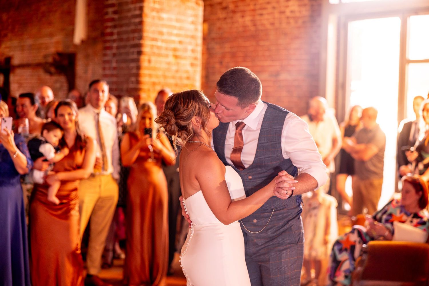 Wedding reception in a rustic brick venue with warm lighting and dancing guests.