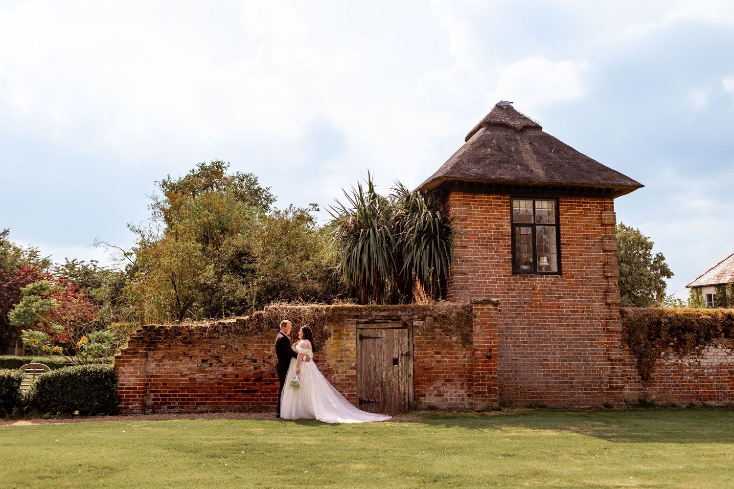 Wedding couple poses in front of historic brick tower and wall in garden setting.