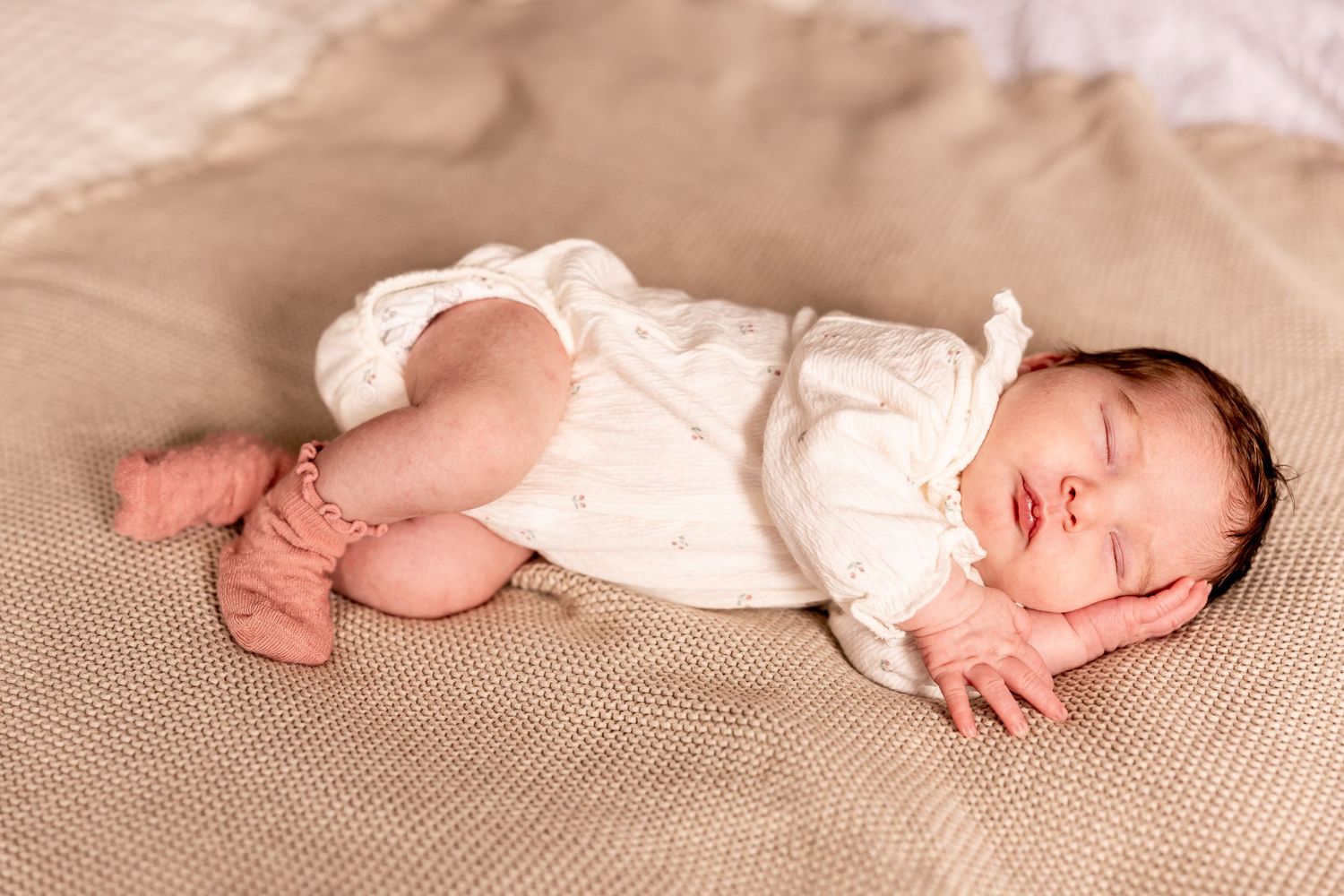 Peaceful newborn baby sleeping on beige blanket wearing white onesie.