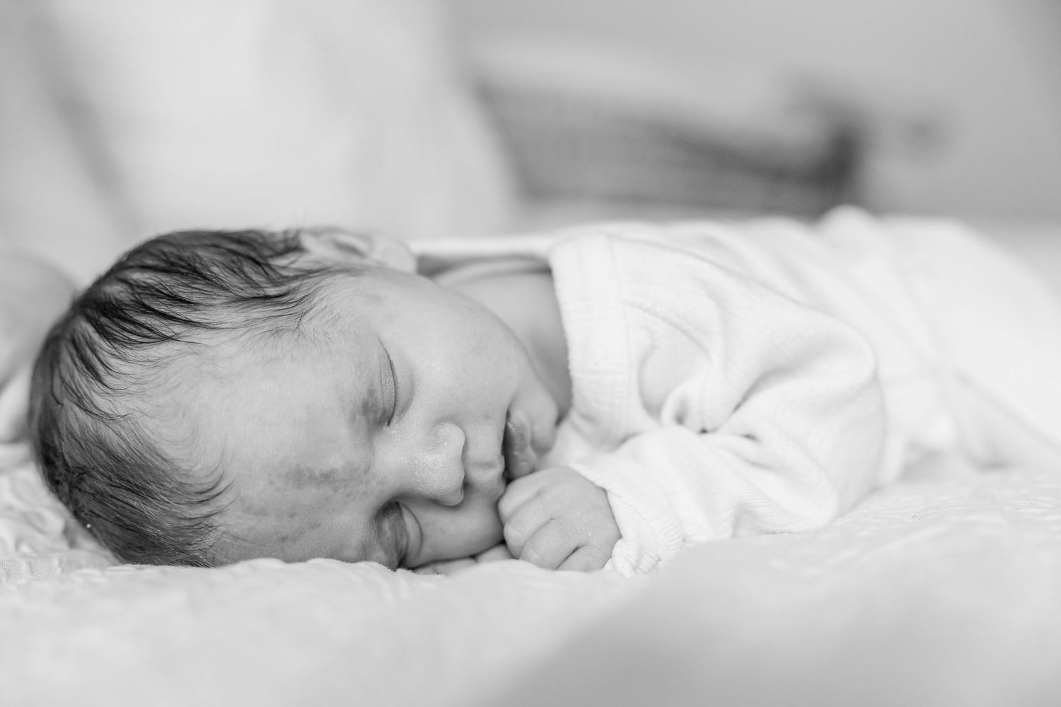 Peaceful sleeping newborn in white outfit captured in black and white.