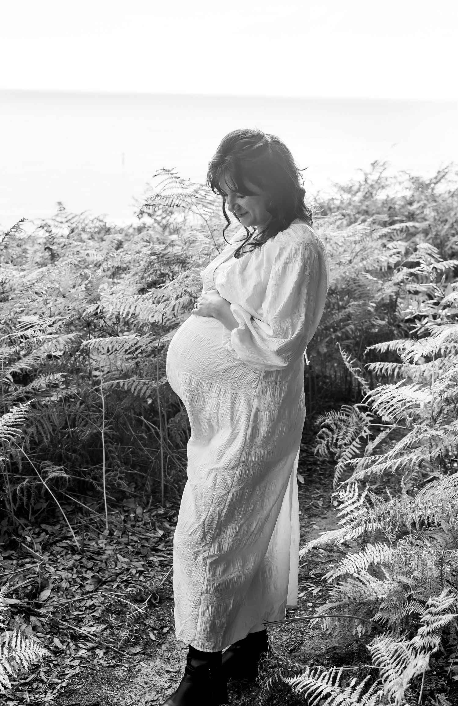 Artistic black and white maternity photo among ferns in nature.