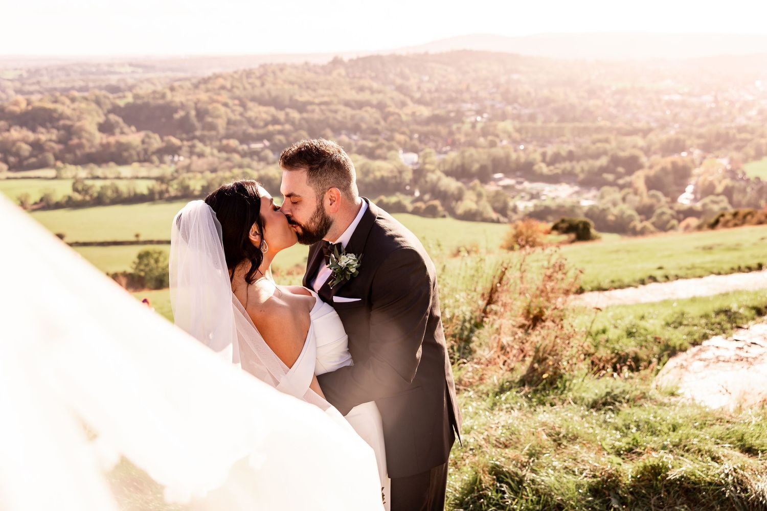 Newlyweds embrace in romantic poses against a scenic countryside backdrop during golden hour.