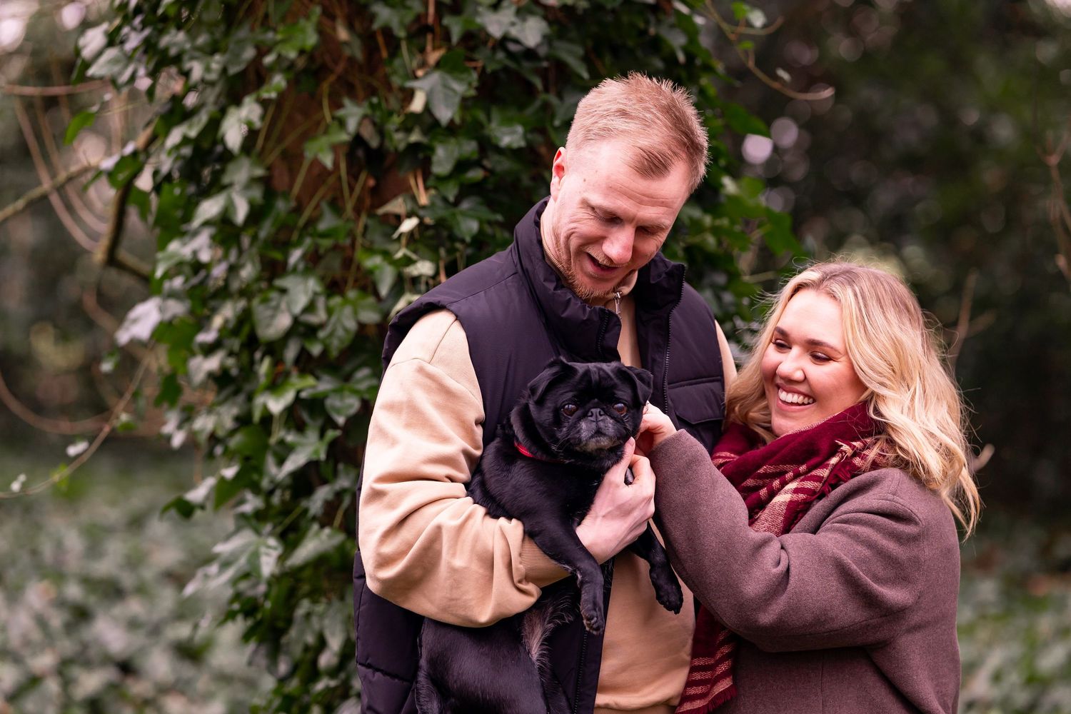 A couple shares a joyful moment while holding their small black dog outdoors.