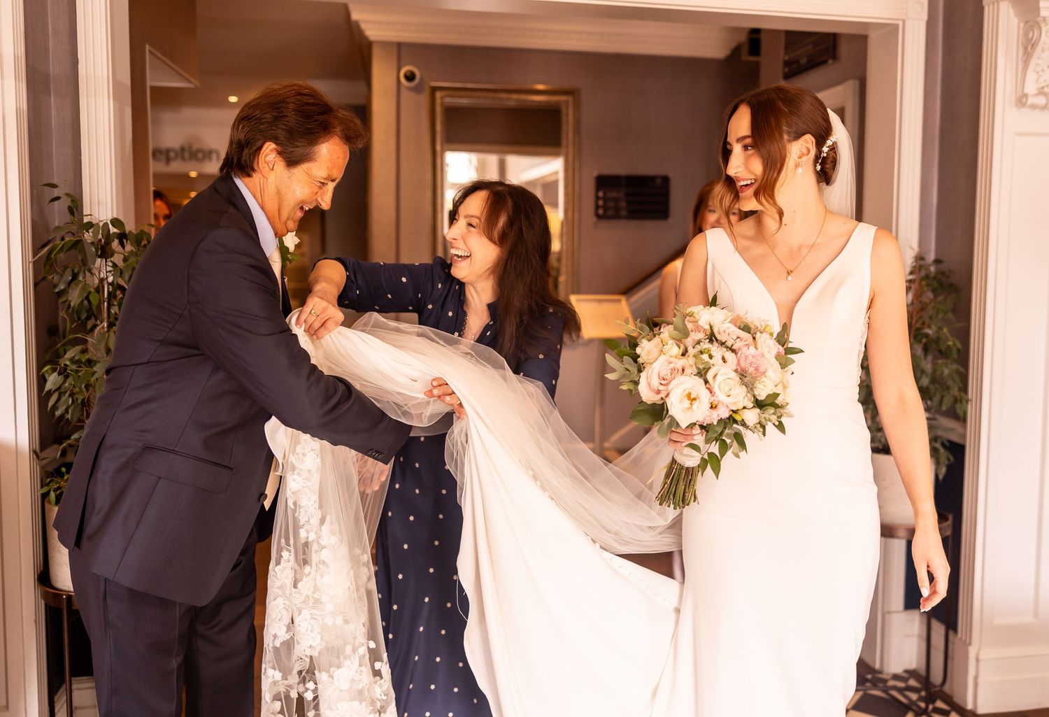 Wedding party celebrates with joyful dancing and embraces at an elegant indoor reception venue.