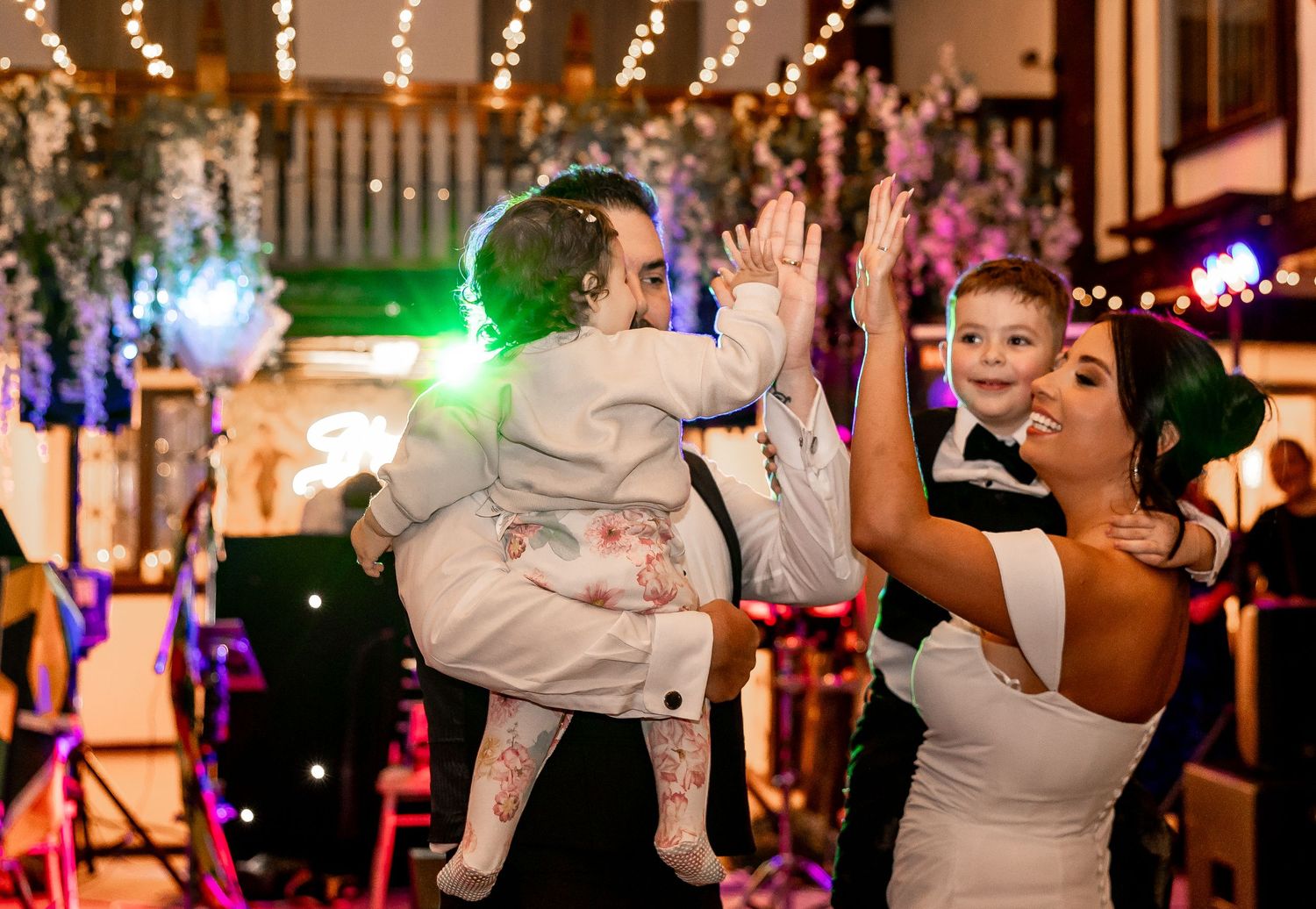 Wedding reception dance floor filled with guests enjoying the celebration under colorful lights.