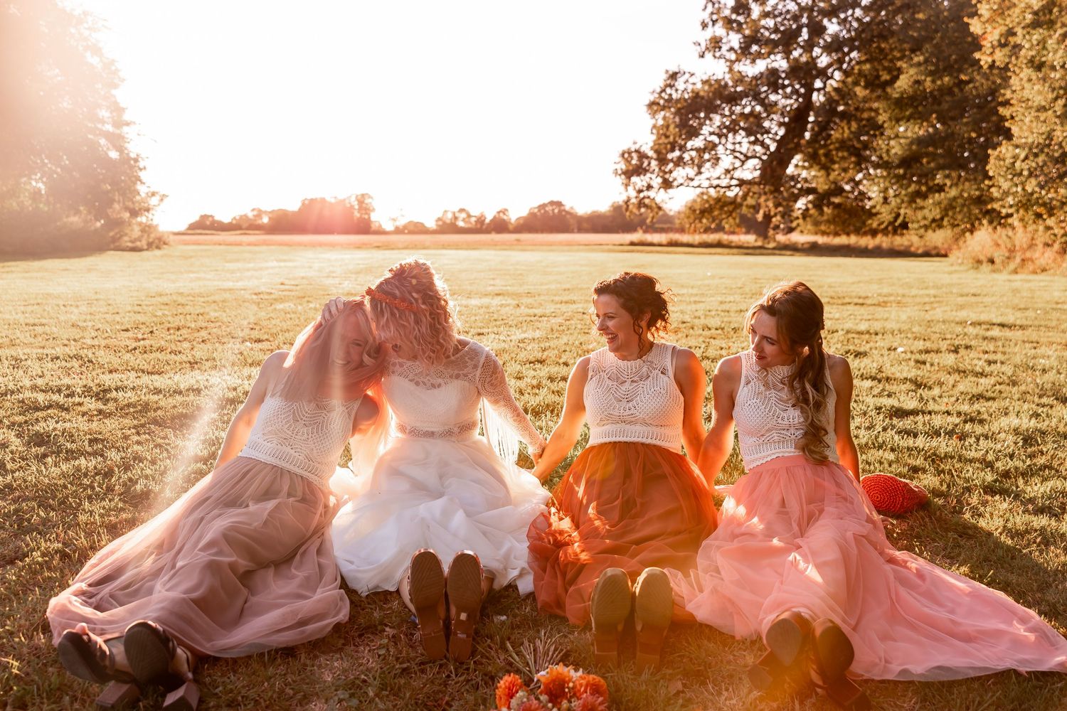 Wedding party in pink dresses relaxing in a sun-drenched field at sunset.