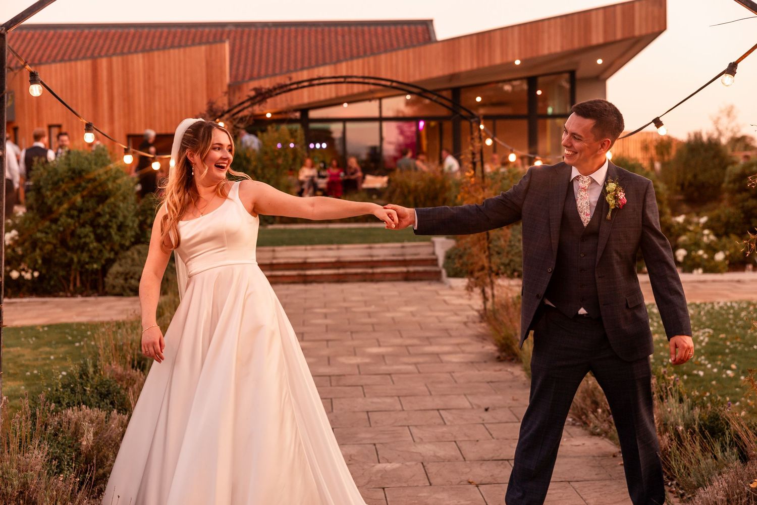 Playful dancing moment between couple on stone patio with modern venue backdrop.