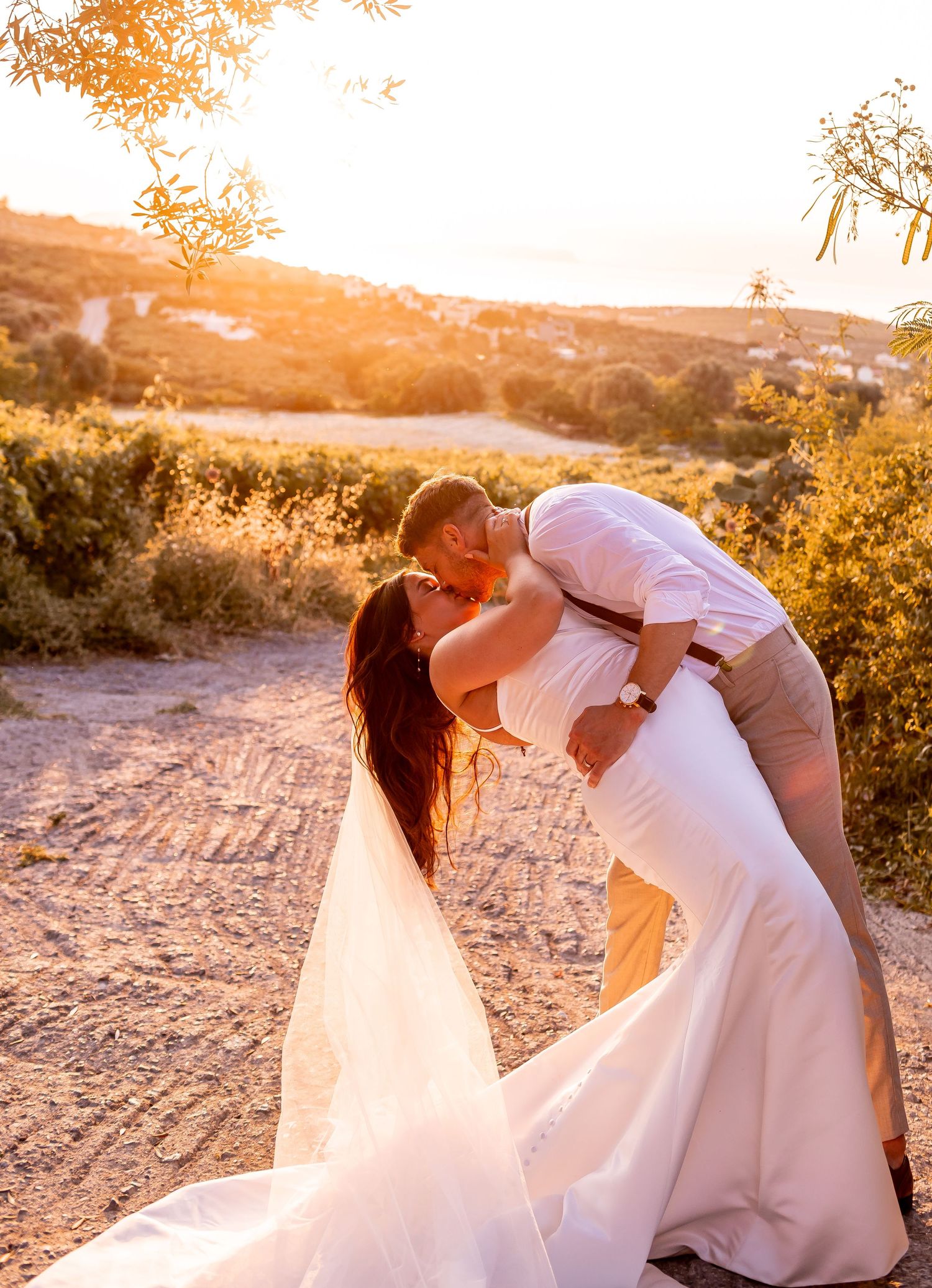 A romantic sunset wedding photo with a couple in an intimate dip pose on a dirt path.