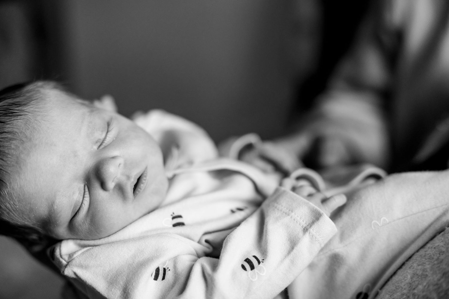 Peaceful sleeping newborn baby wearing striped onesie in black and white portrait.