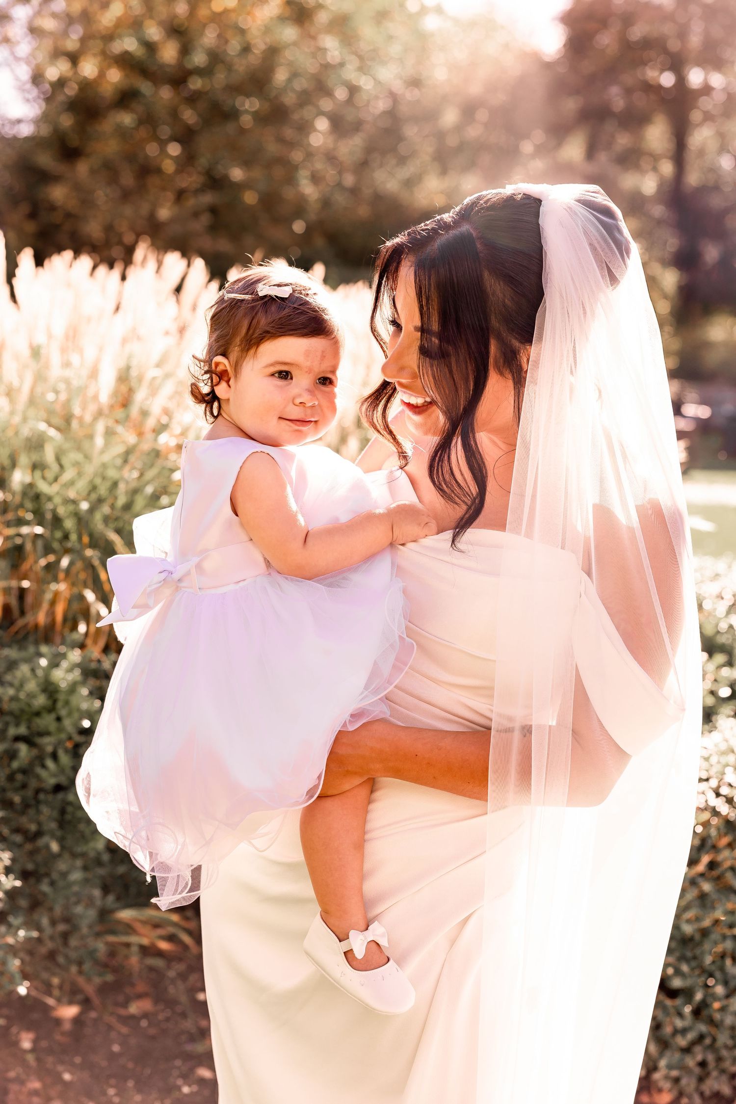 Sweet moment between bride in white dress and small child in garden setting at sunset.
