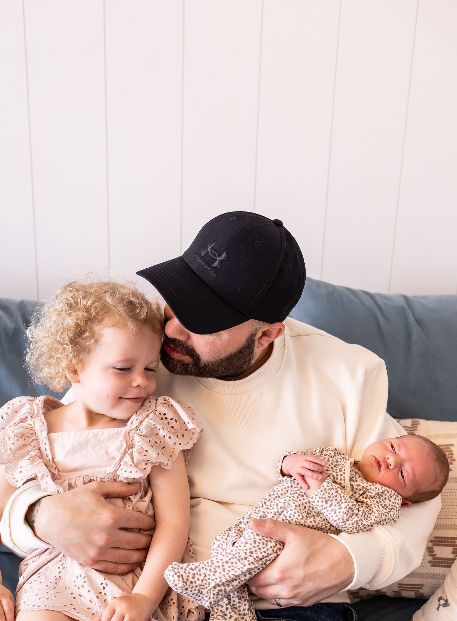 Father in casual wear holding two children in matching floral dresses.
