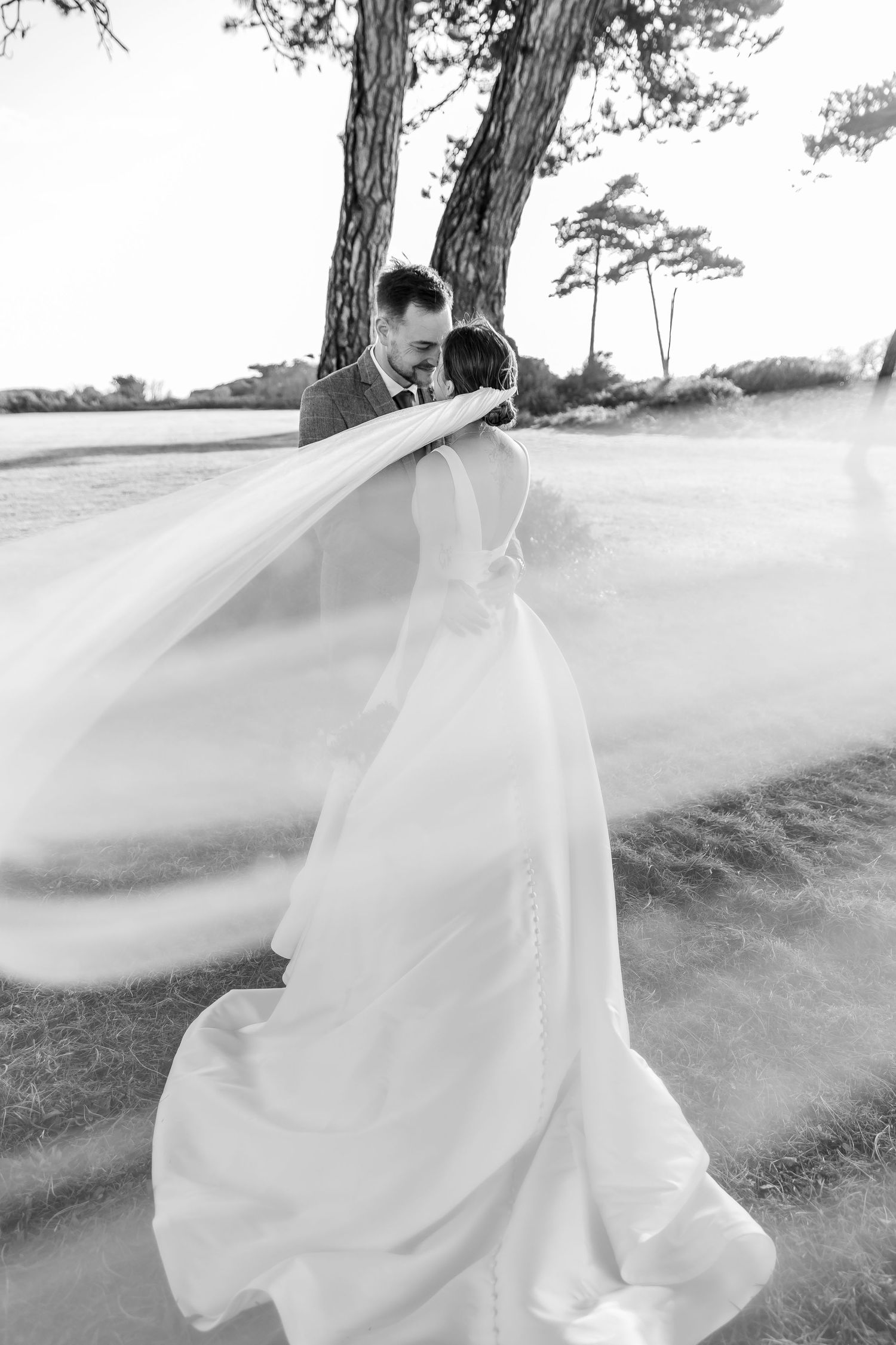Ethereal black and white photo of bride's flowing veil caught in wind among pine trees.