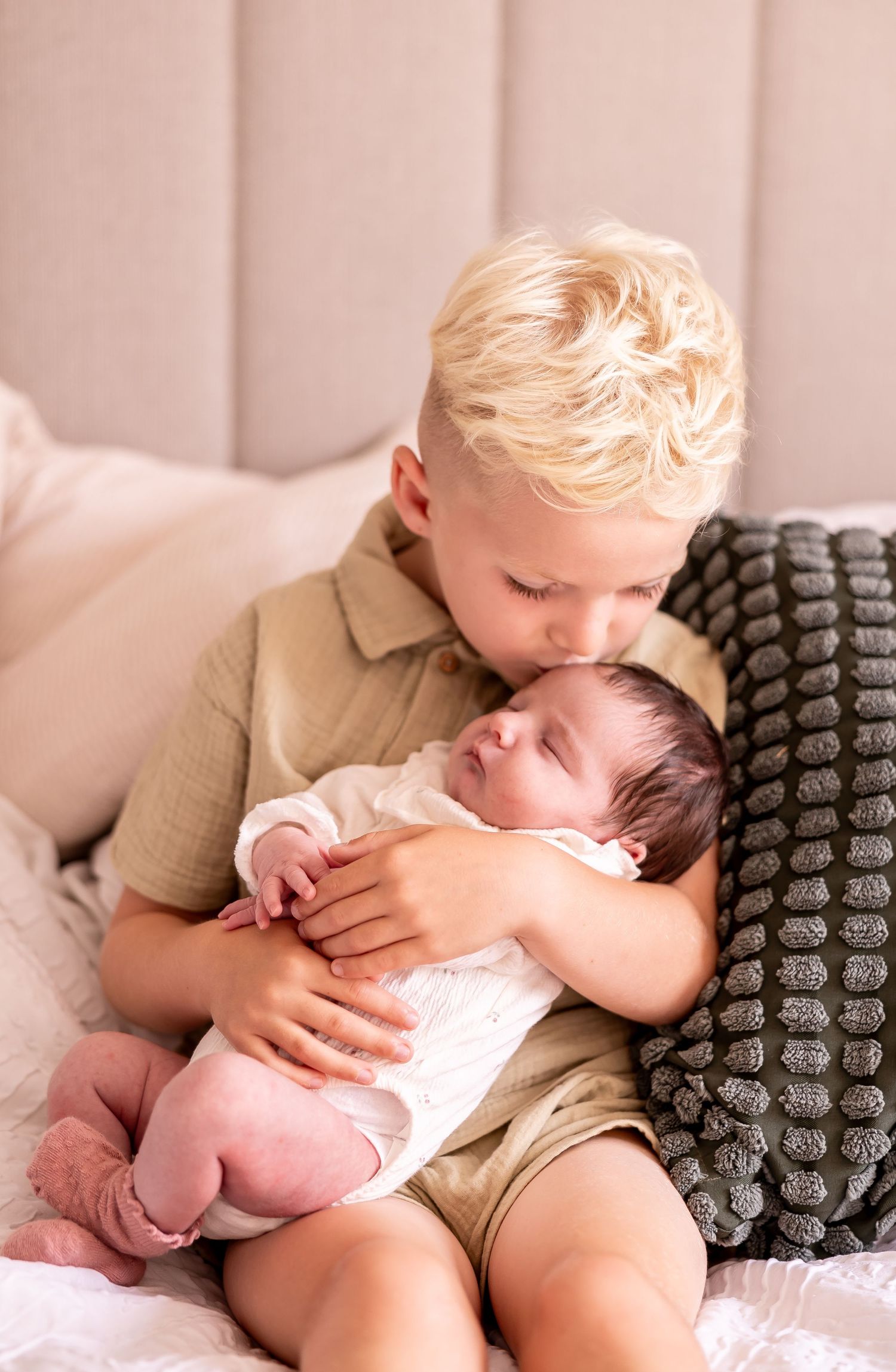 Tender moment between siblings as older child holds and kisses newborn baby.