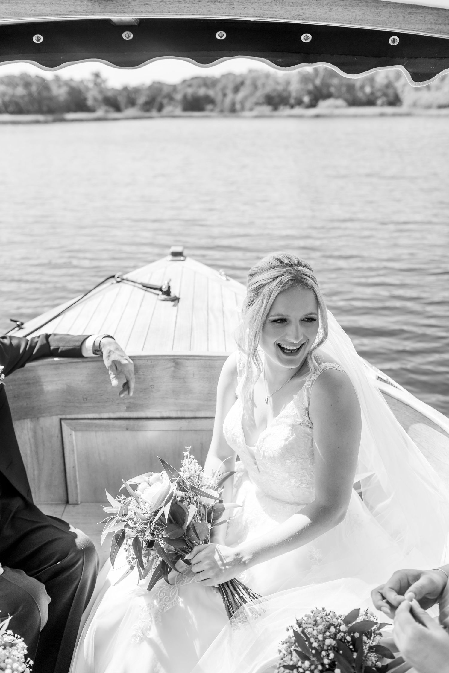 Wedding party laughing together in vintage wooden boat on lake.