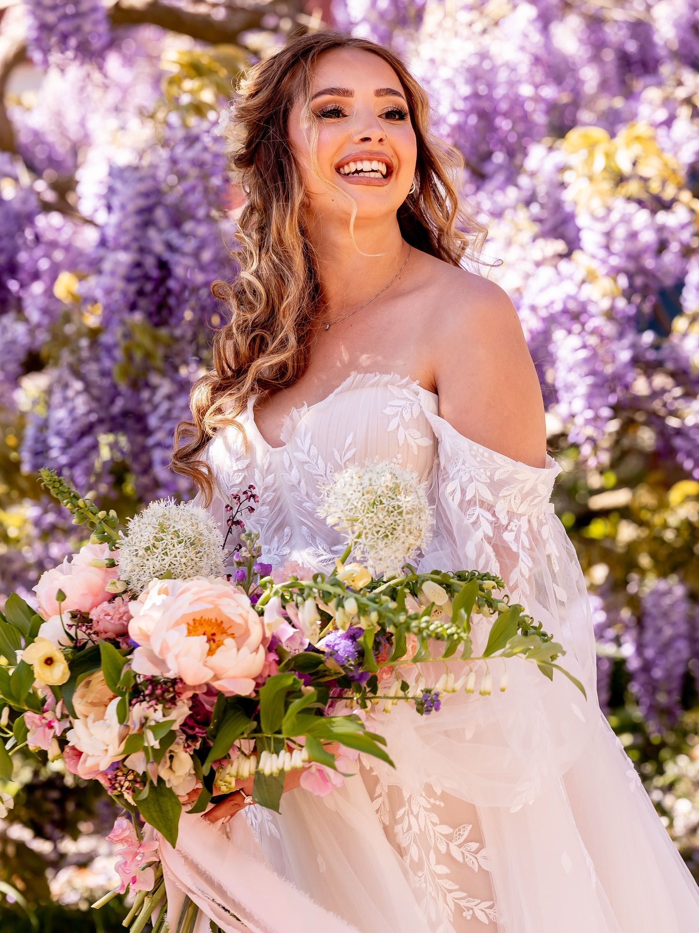 Elegant bridal portrait amidst blooming purple wisteria with spring bouquet.
