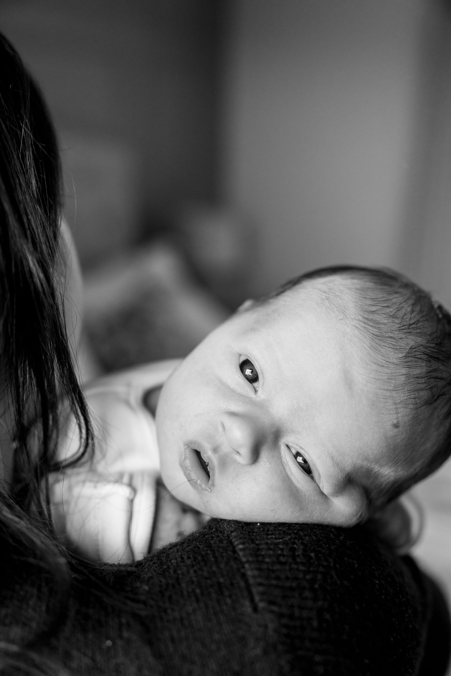 Black and white portrait of alert newborn baby resting on caregiver's shoulder.