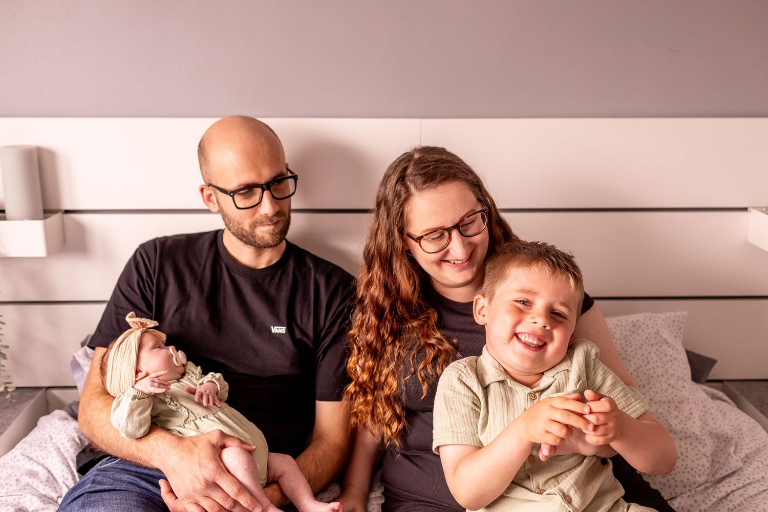 Happy family lounging together on bed with newborn baby.