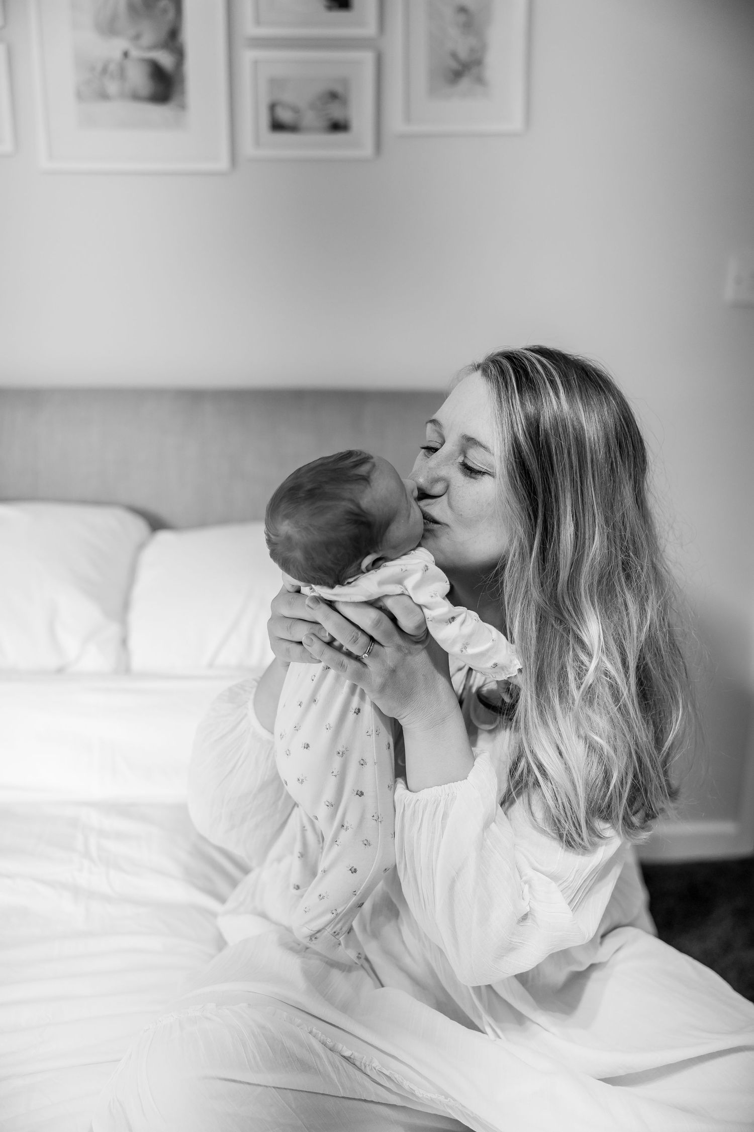 A tender black and white moment of a parent kissing their newborn baby in bed.