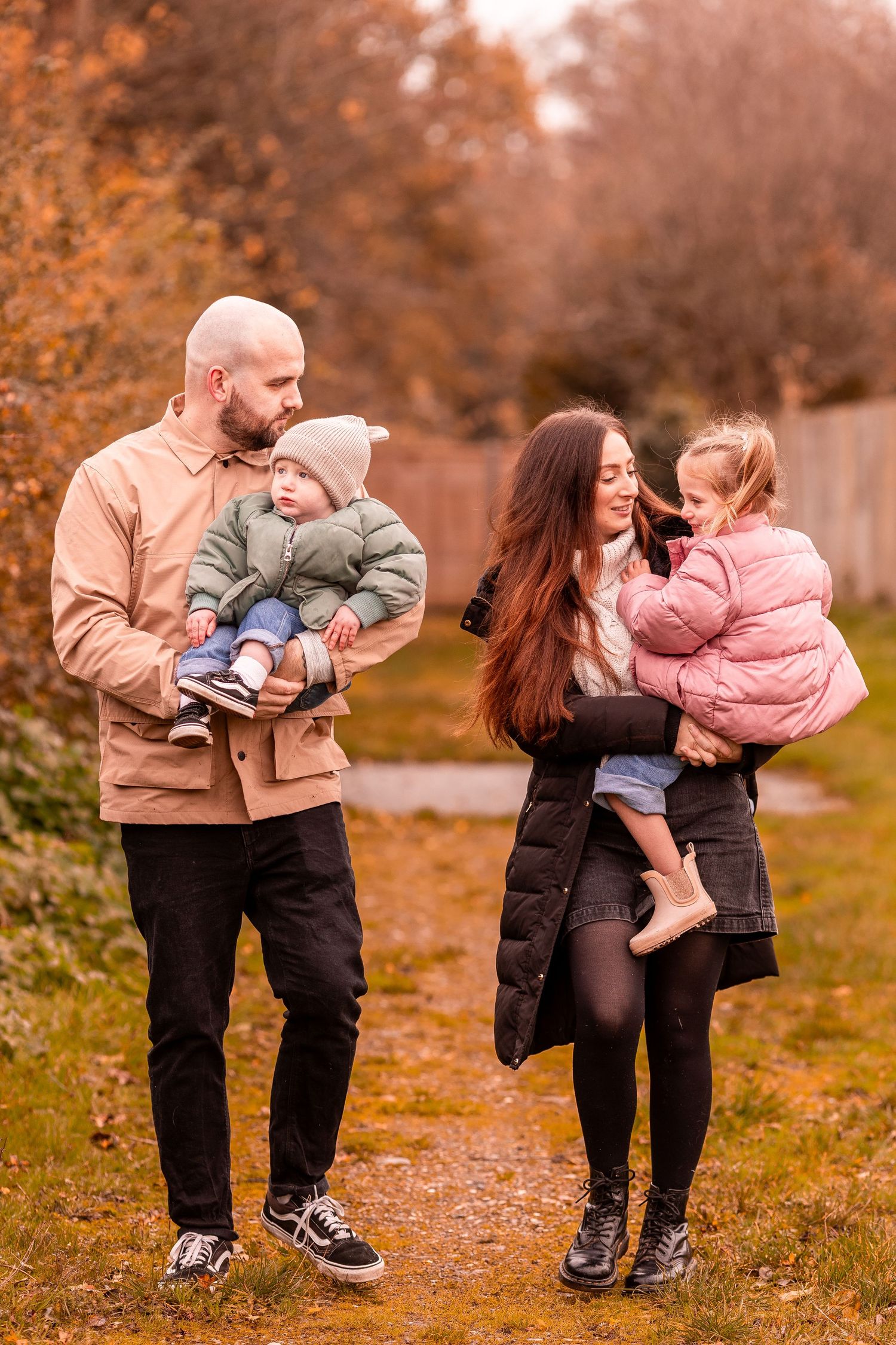 A family enjoys a walk together on a fall day with their small children bundled up in warm clothing.