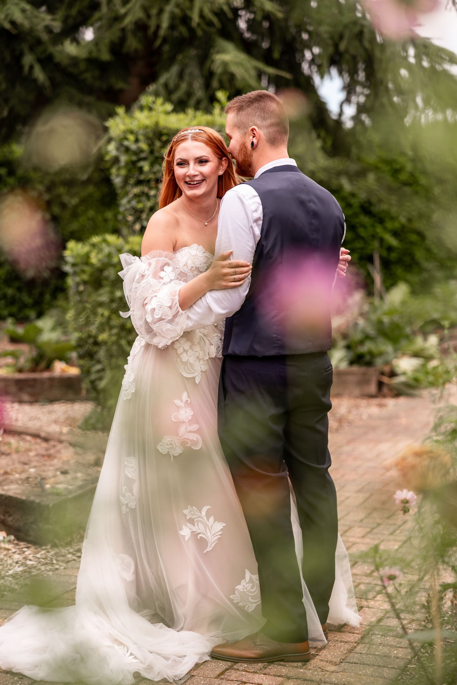 Couple shares a romantic garden moment surrounded by greenery in elegant wedding attire.