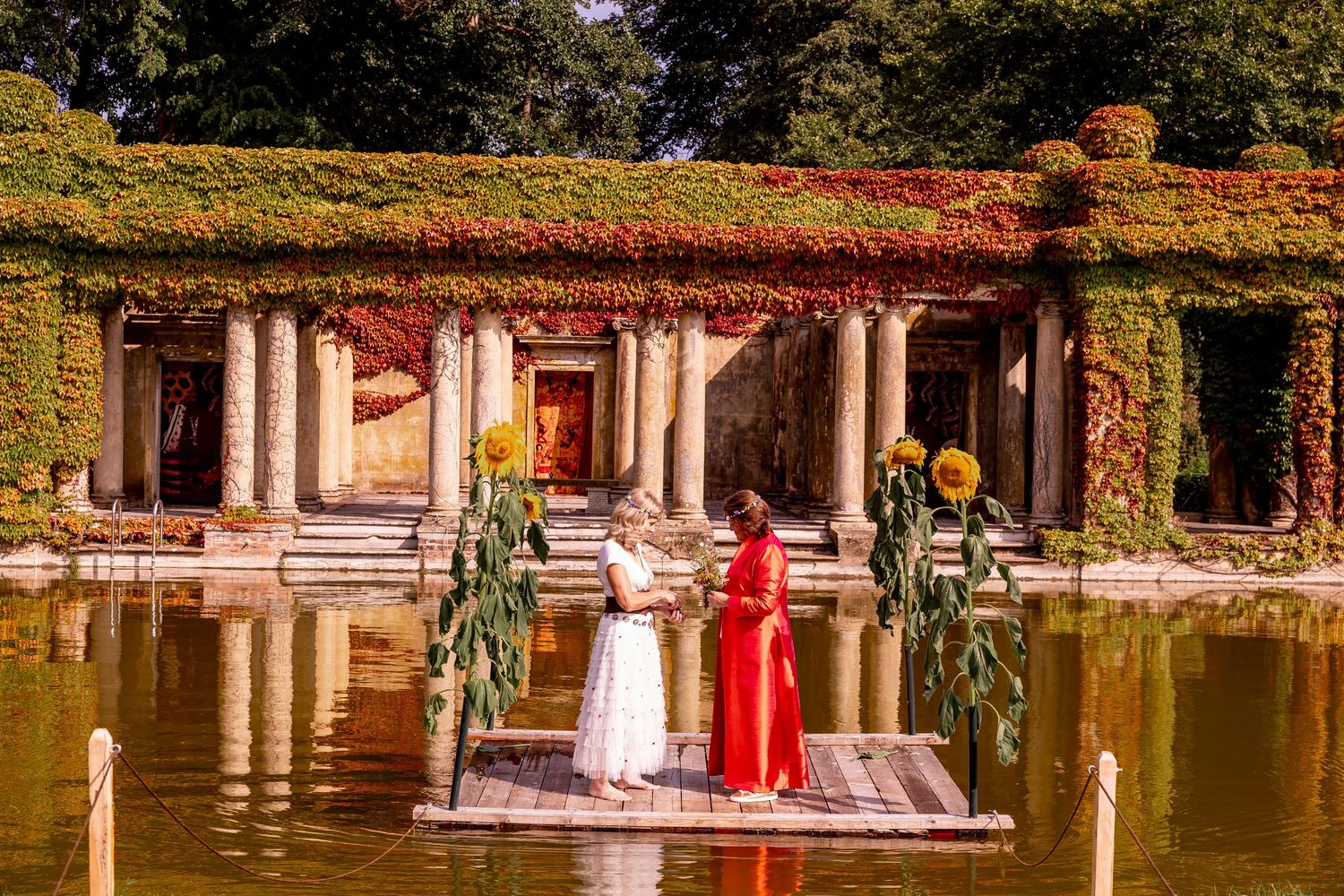 Outdoor wedding venue with stone columns and red drapery in a garden setting.
