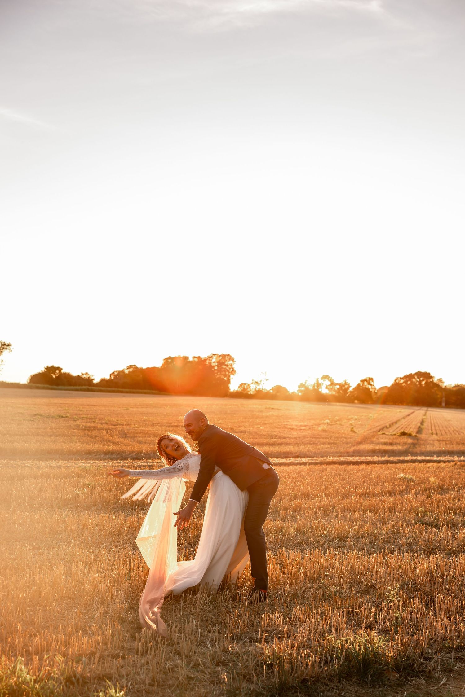 Romantic sunset dip pose in golden wheat field with flowing veil.