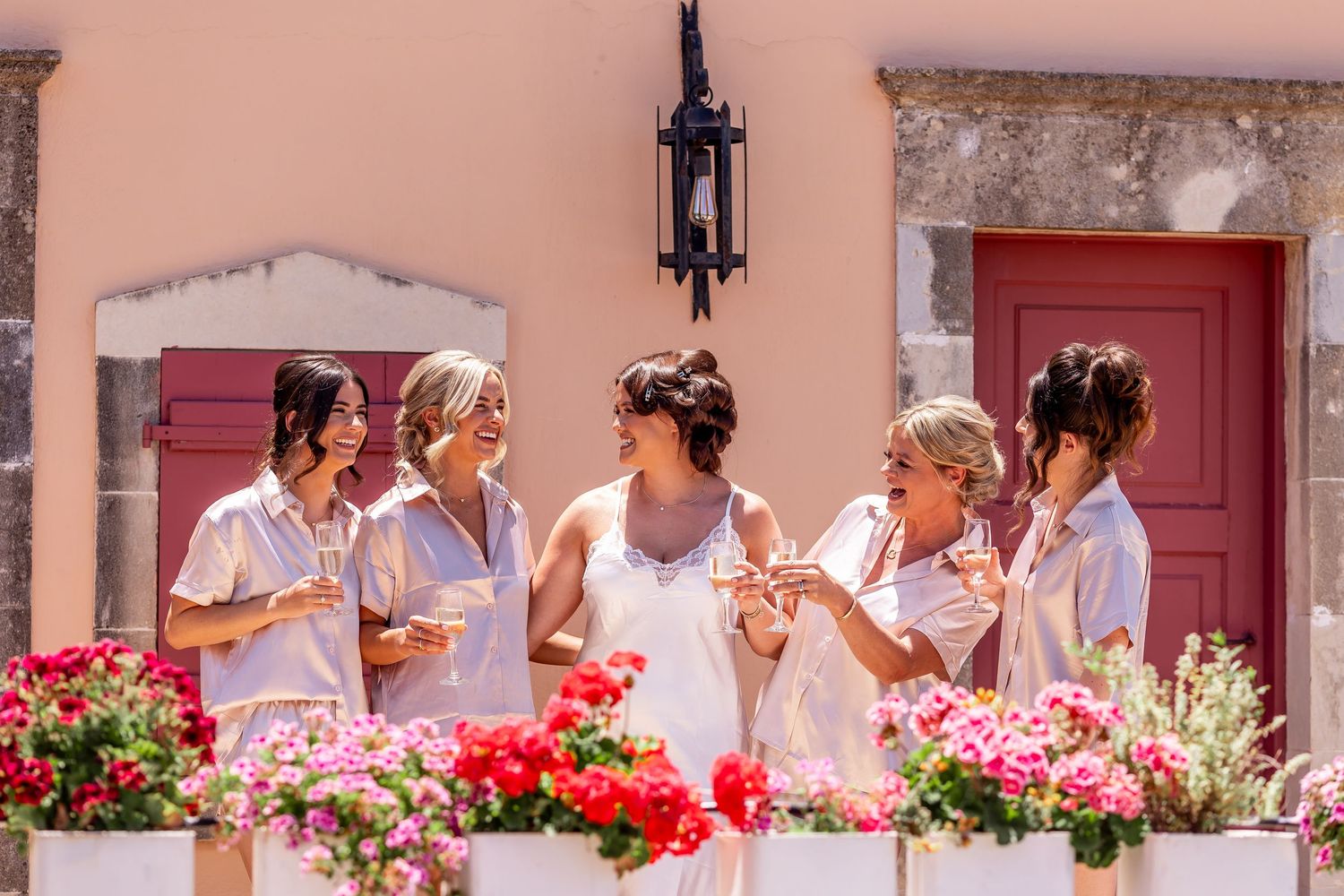 Wedding party gathered outside pink Mediterranean building with red flowers in window boxes.