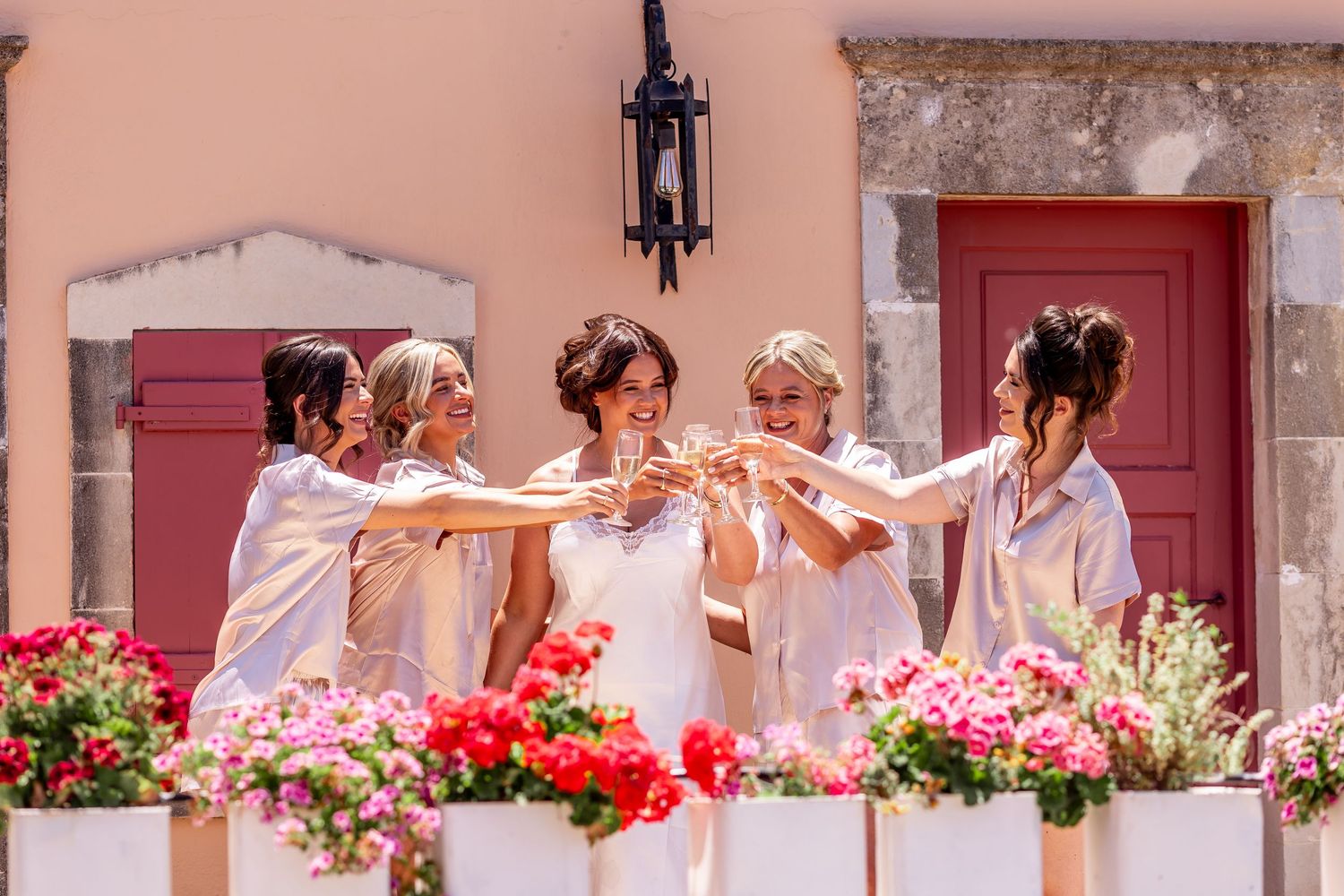 A joyful group in matching white robes celebrates on a balcony decorated with colorful flowers.