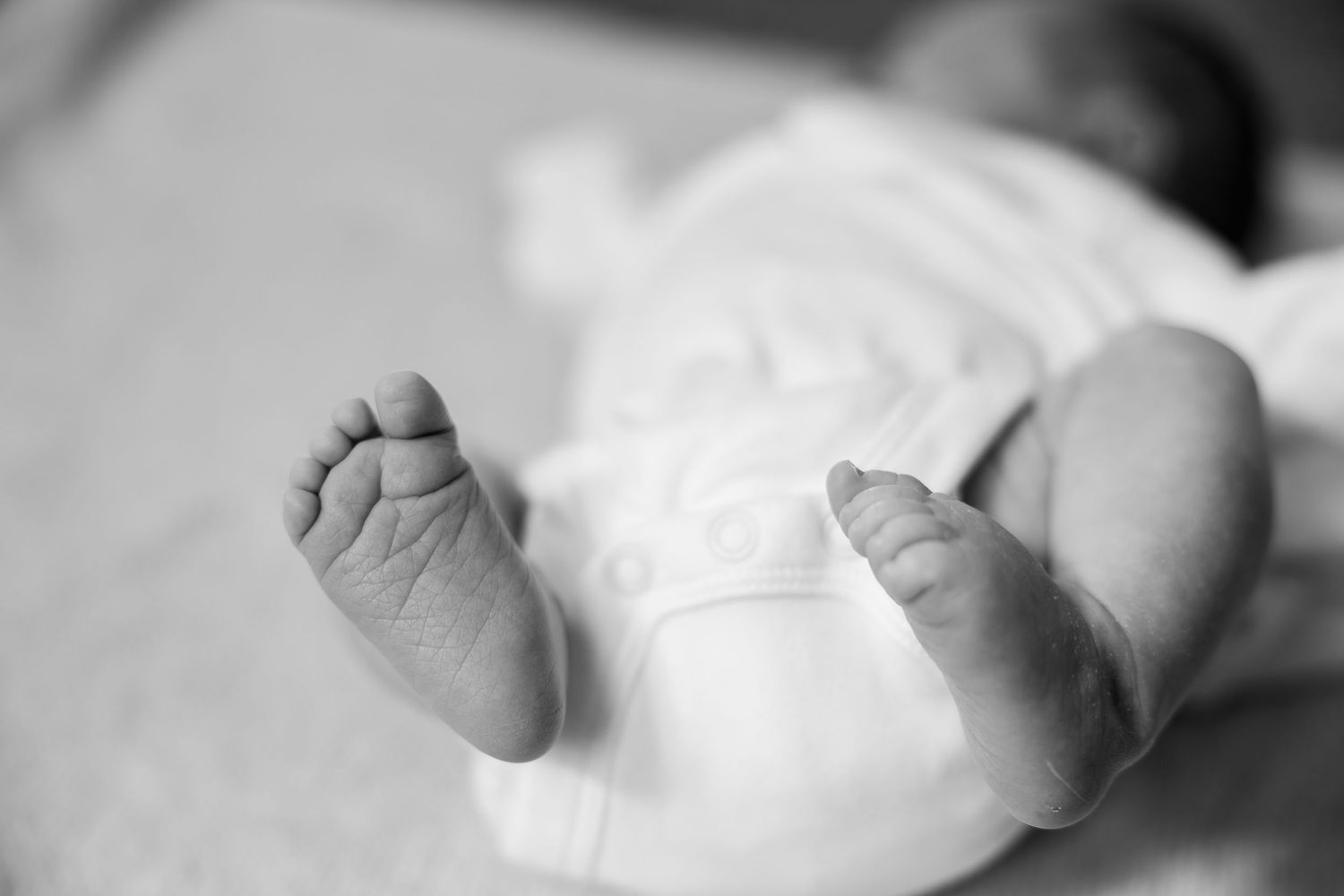 Close-up black and white photo of tiny newborn baby feet against white fabric.