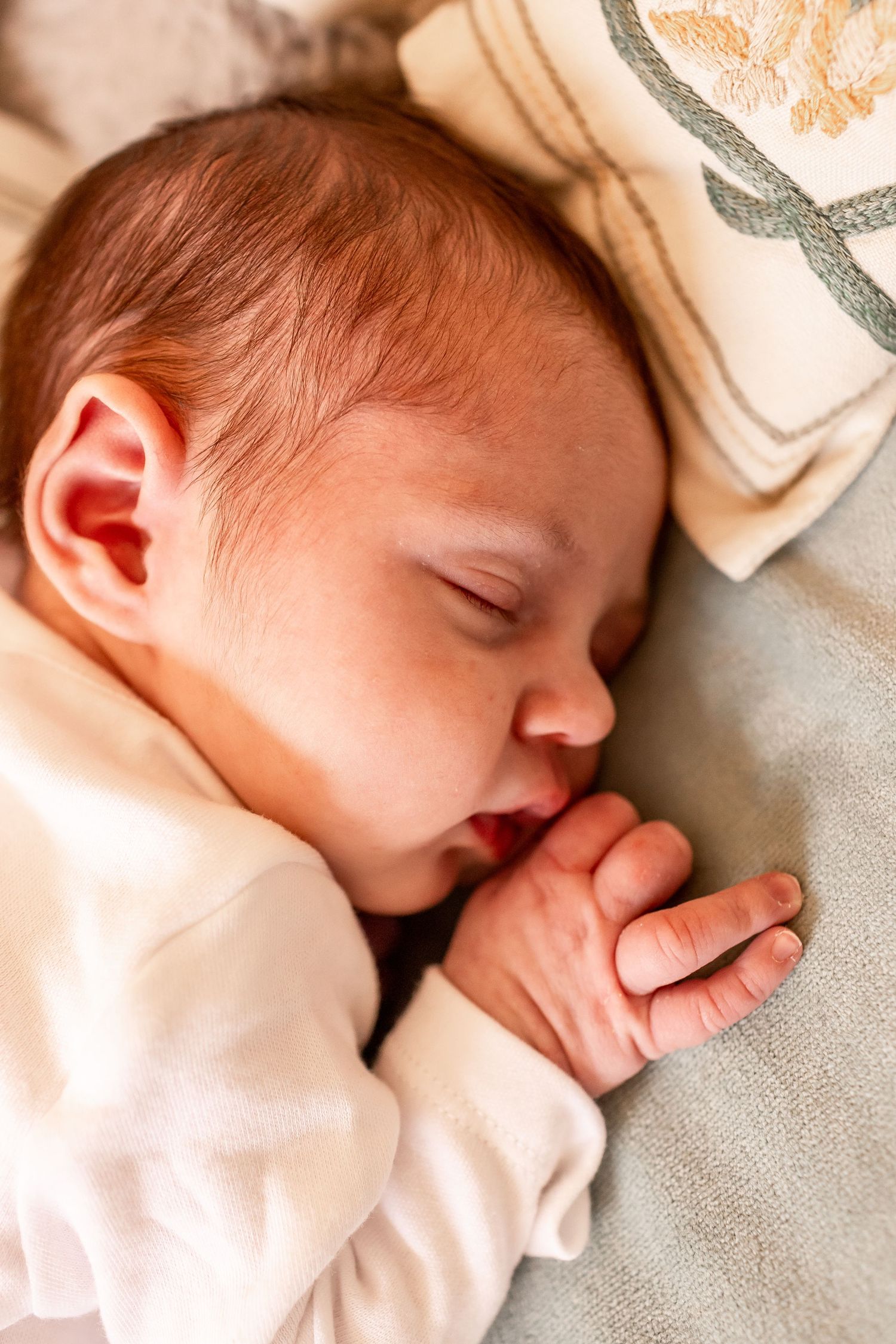 Close-up of sleeping baby with tiny hands clasped near face.